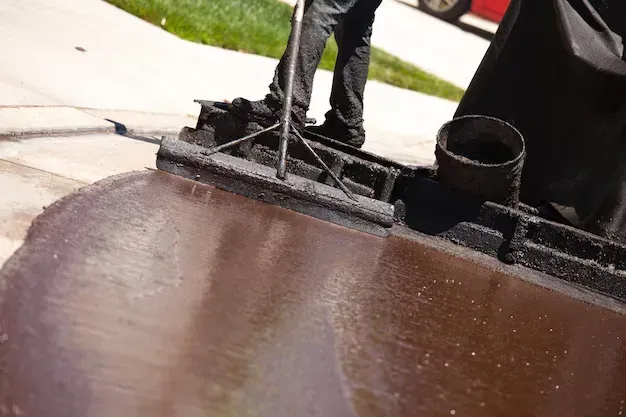 Worker applying tar coating on foundation surface to seal against moisture and prevent water intrusion