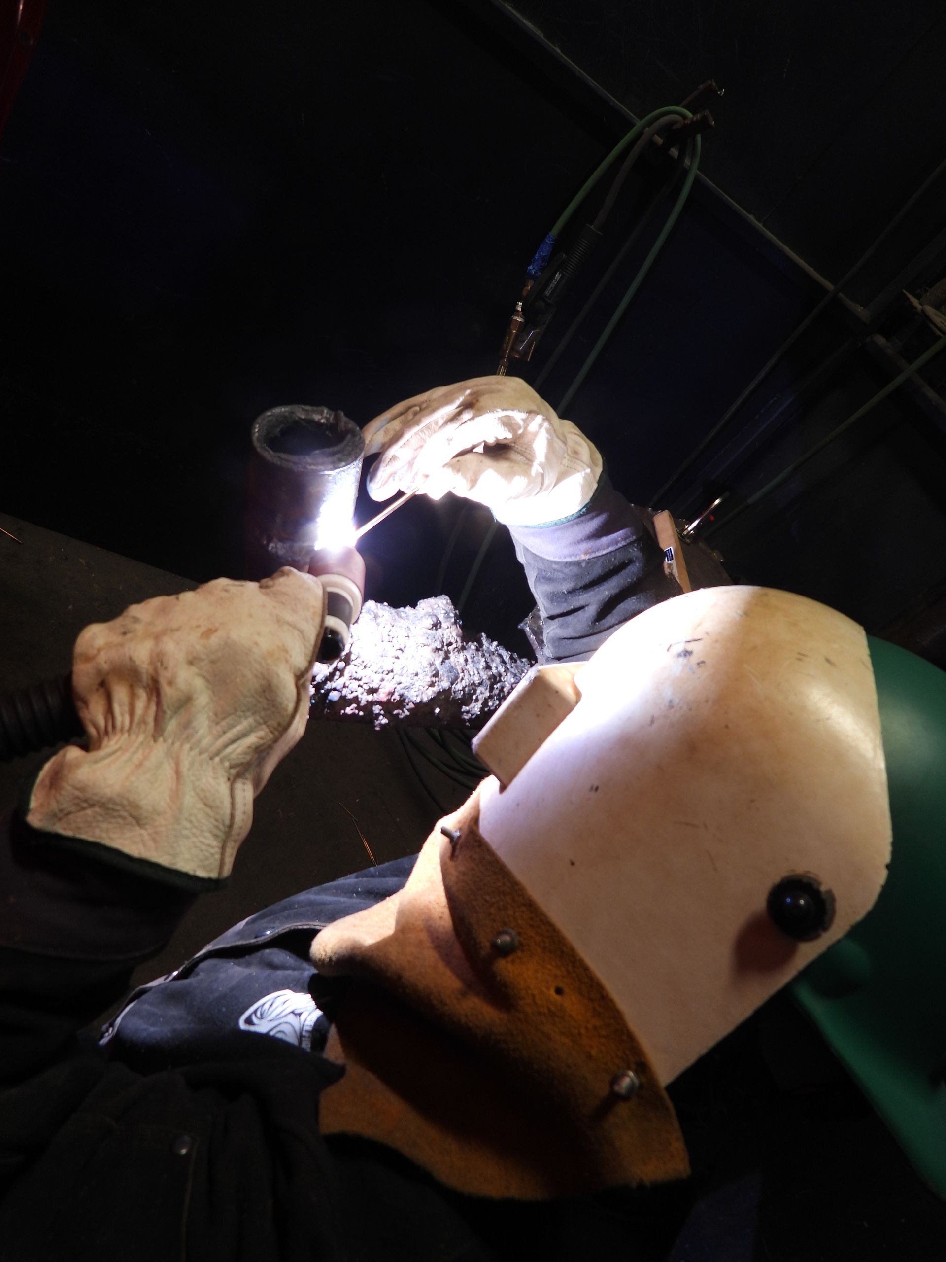 A person wearing a welding helmet is welding a piece of metal