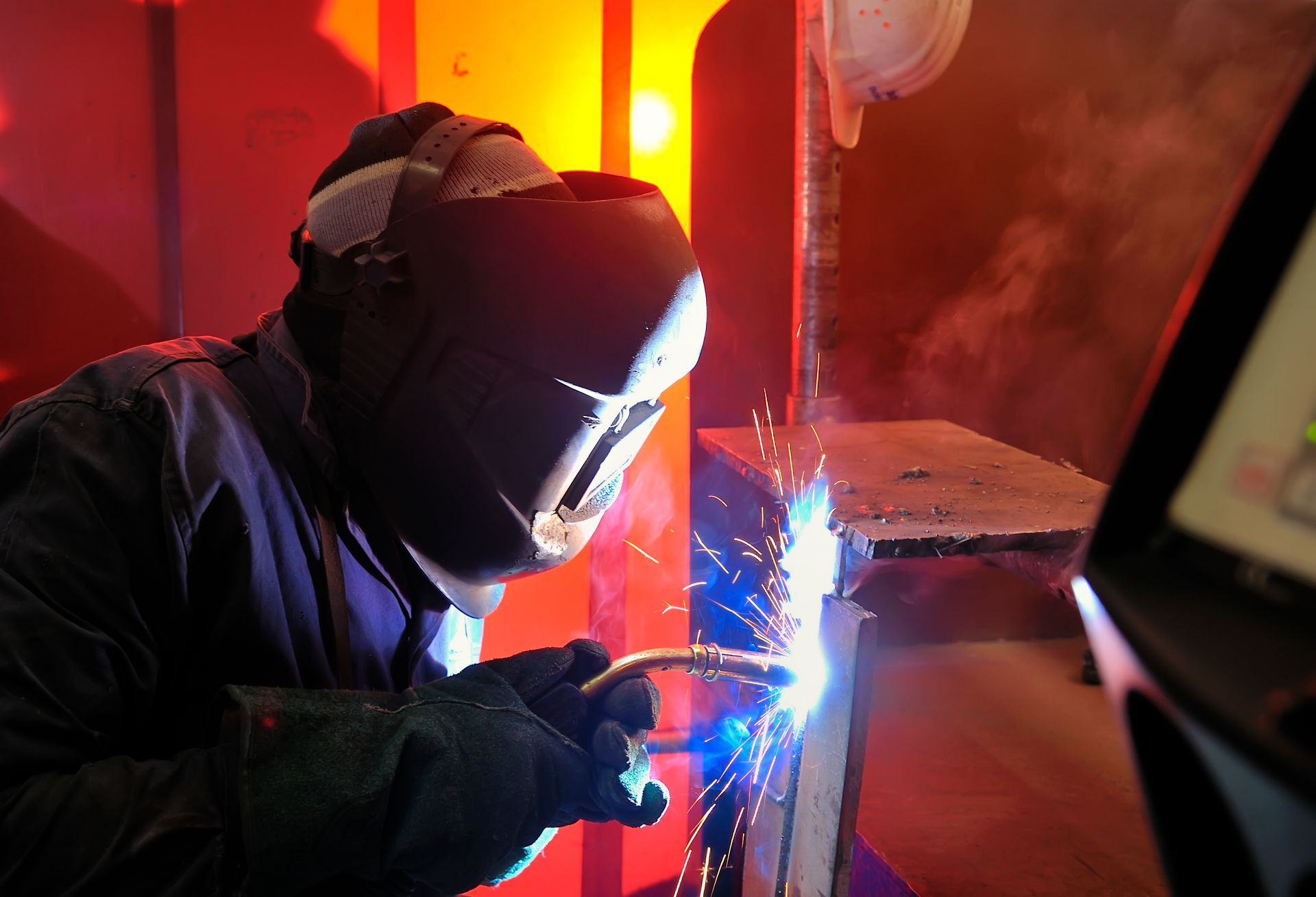 A man wearing a welding mask is welding a piece of metal.