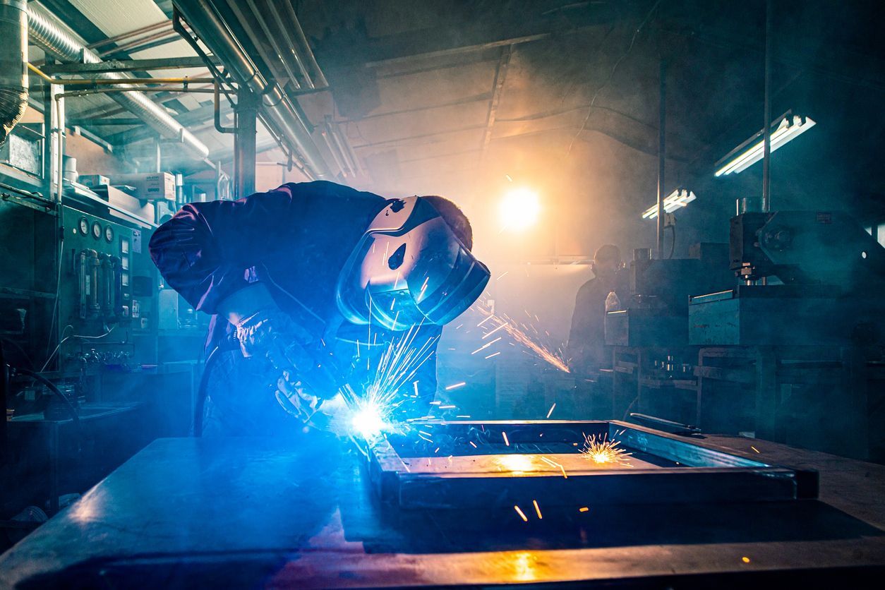 A man is welding a piece of metal in a factory.