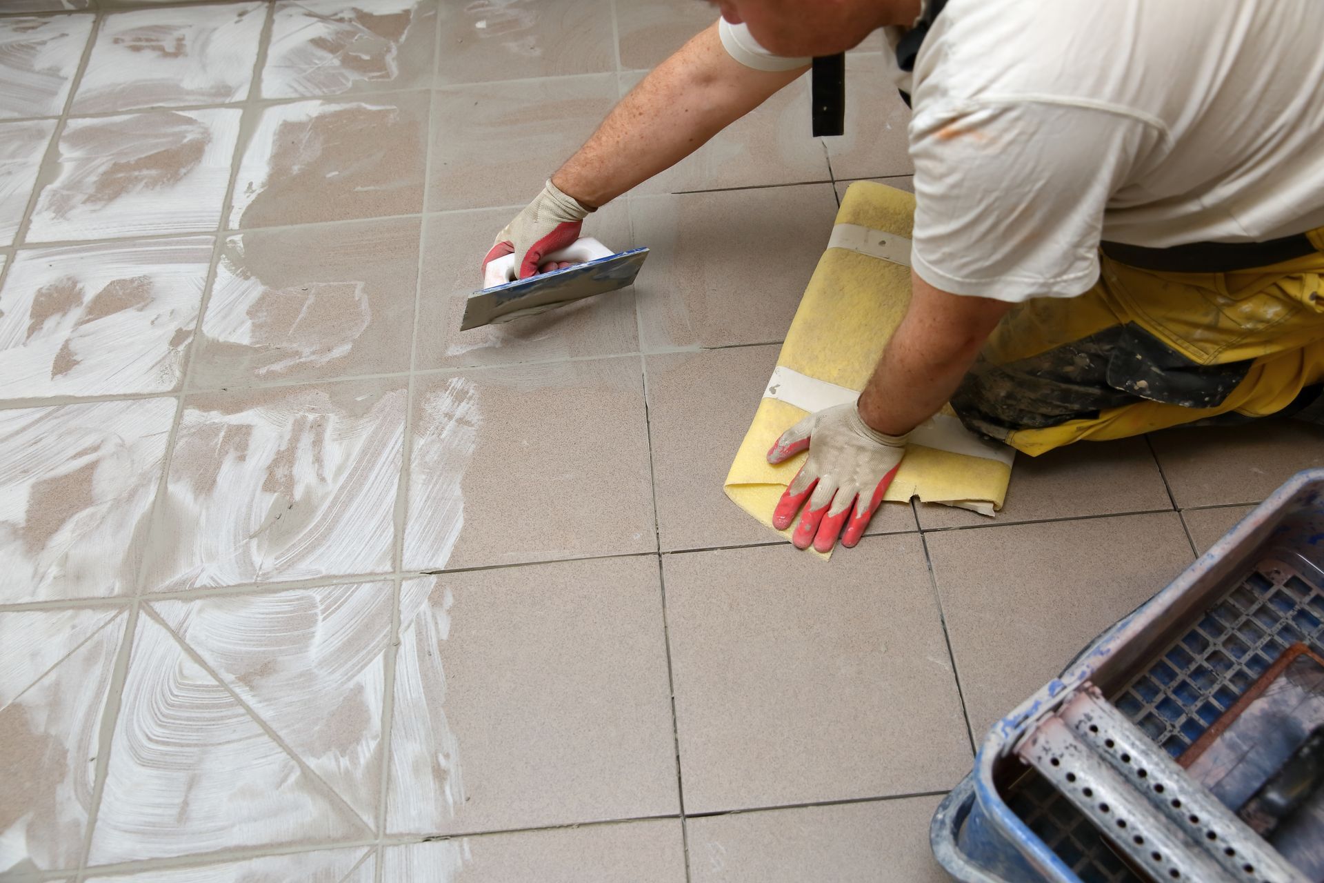 A man is kneeling on the floor using a trowel.
