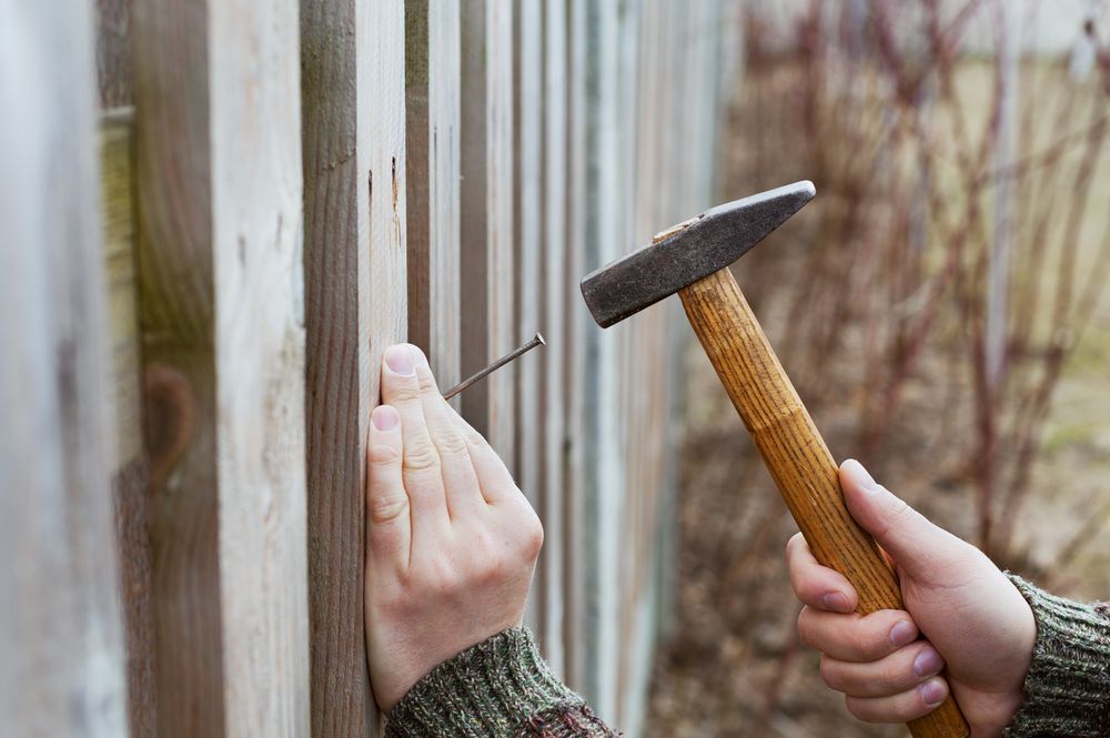A person is hammering a nail into a wooden fence.