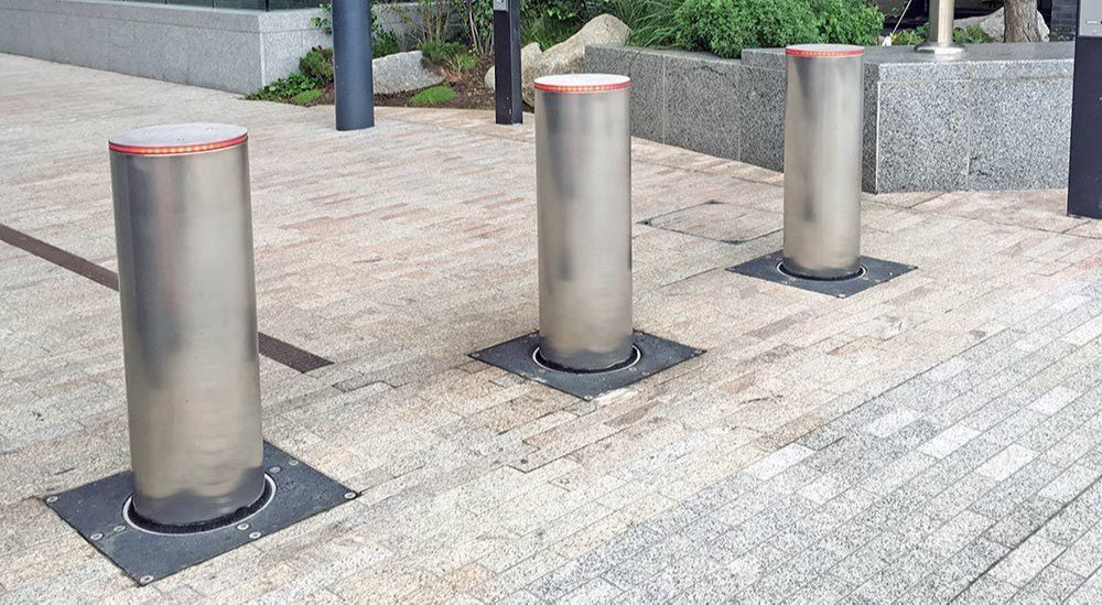 A row of stainless steel poles are sitting on a brick sidewalk.
