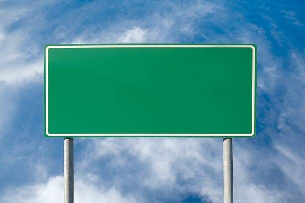 An empty green highway sign against a cloudy blue sky.