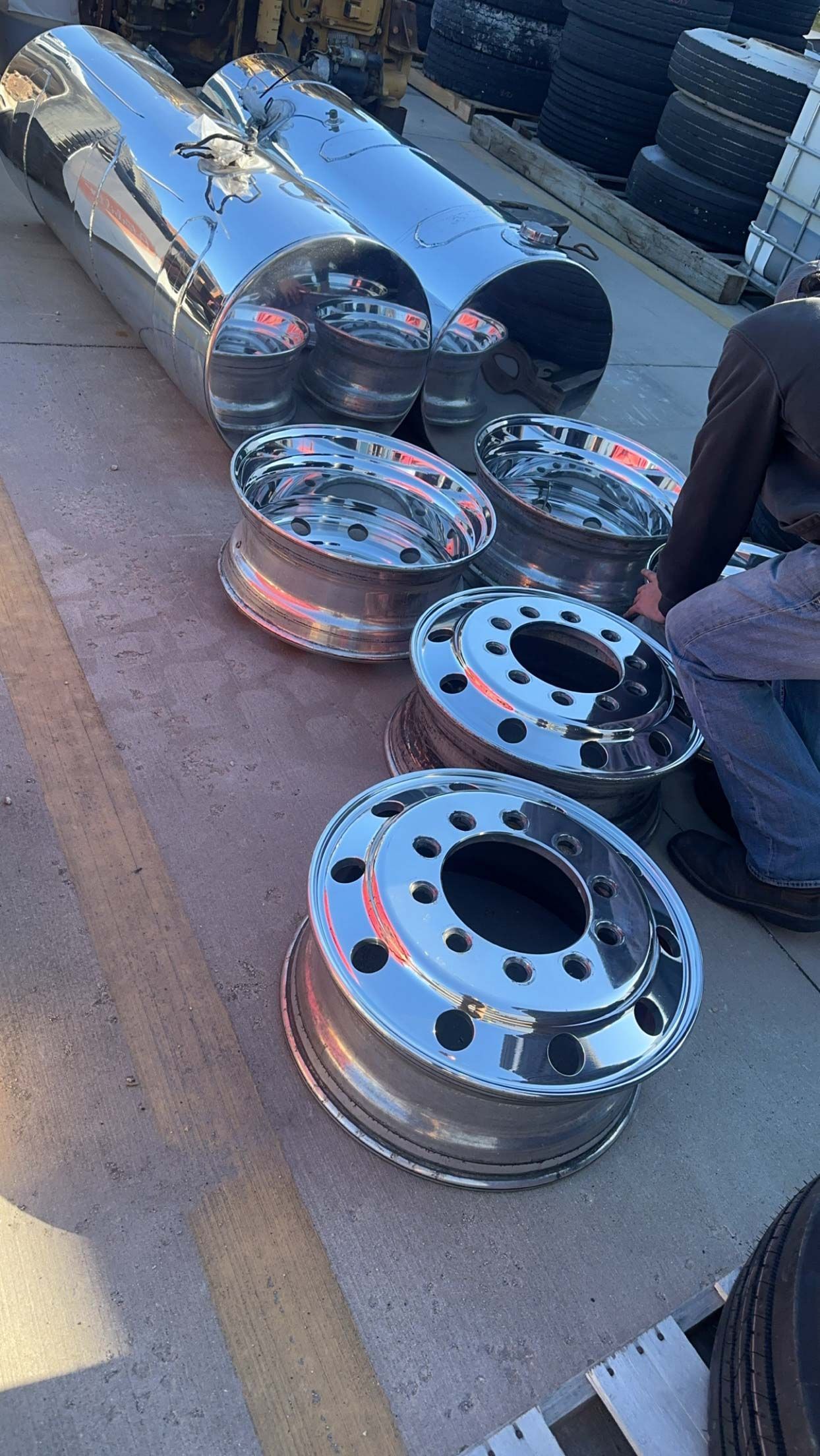 A man is kneeling down next to a row of chrome wheels after receiving metal polishing.