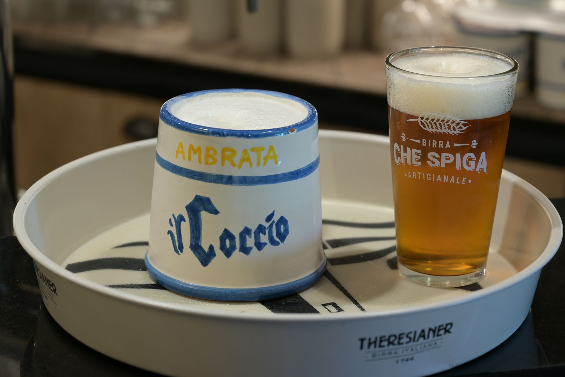 Due bicchieri da birra personalizzati su un vassoio bianco, uno vuoto e l’altro pieno di birra.