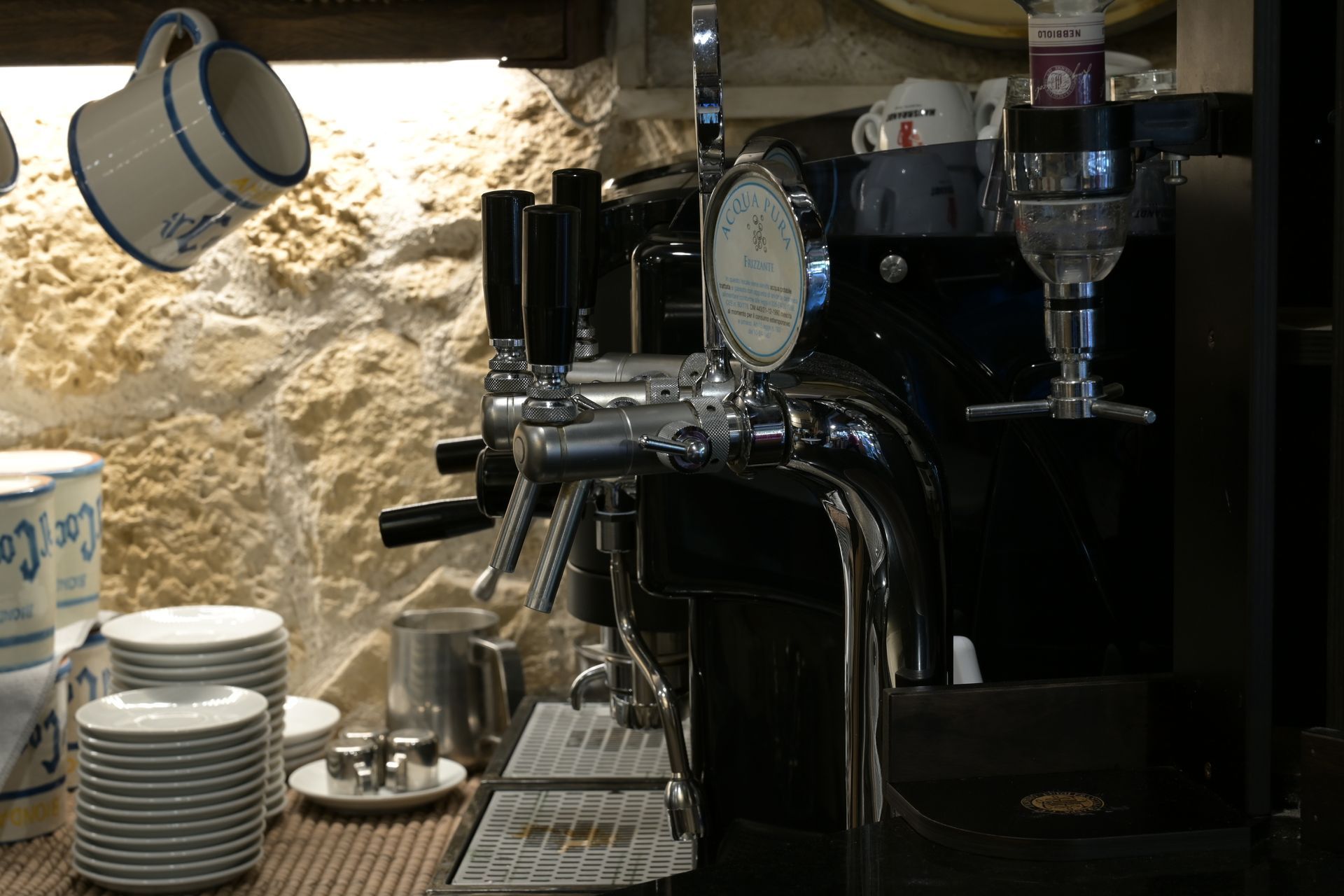 Macchina del caffè con tazze e piattini su un bancone accanto a un muro di pietra