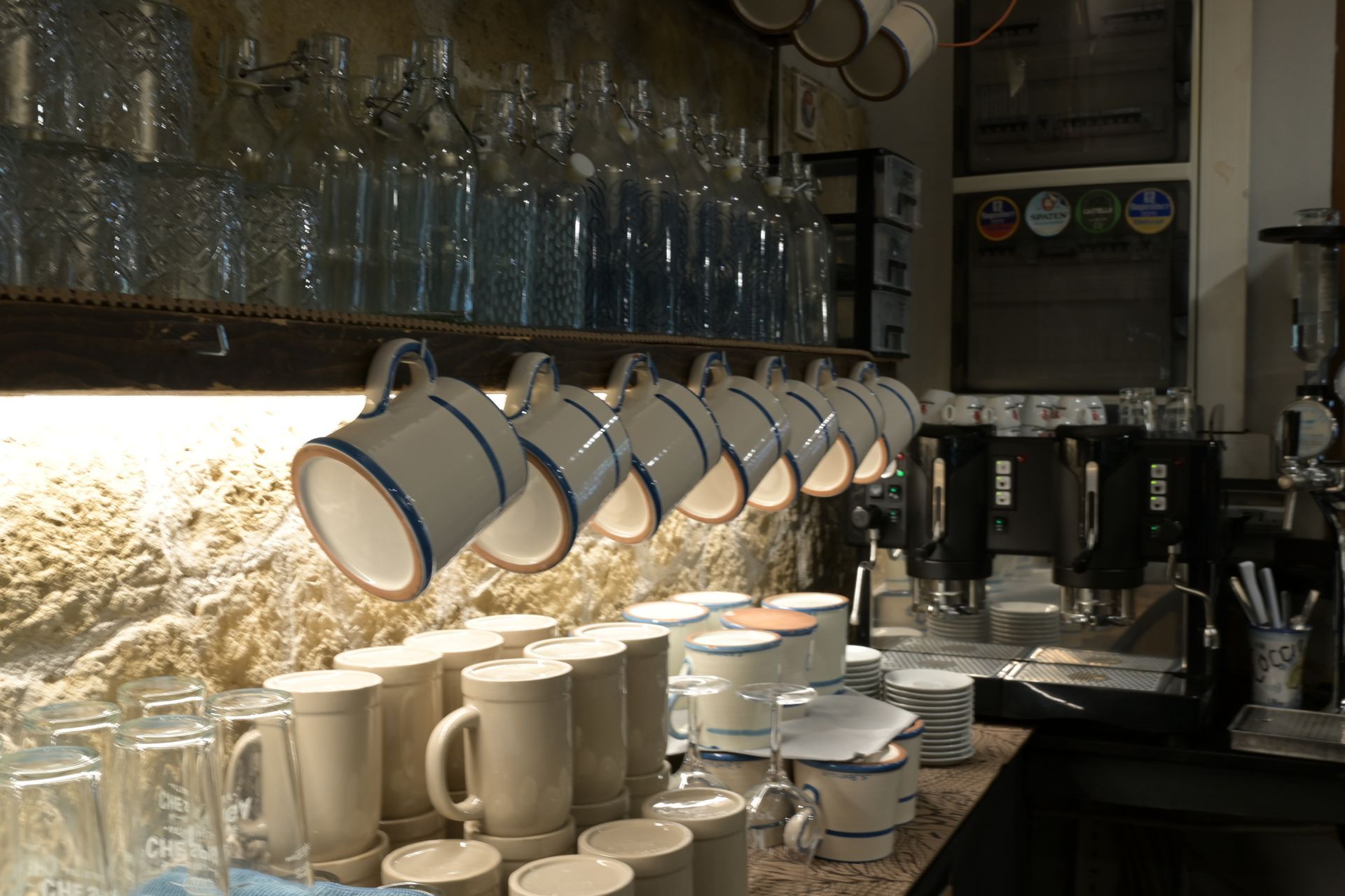Bancone del caffè con tazze appese, piatti impilati e file di bottiglie di vetro sugli scaffali