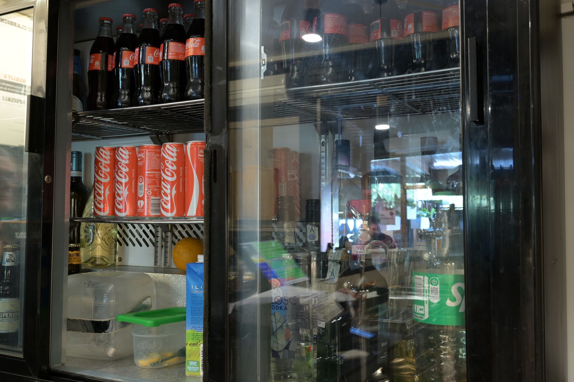 Vetrina refrigerata con bottiglie di Coca-Cola, lattine di bibite e bevande assortite dietro il vetro.