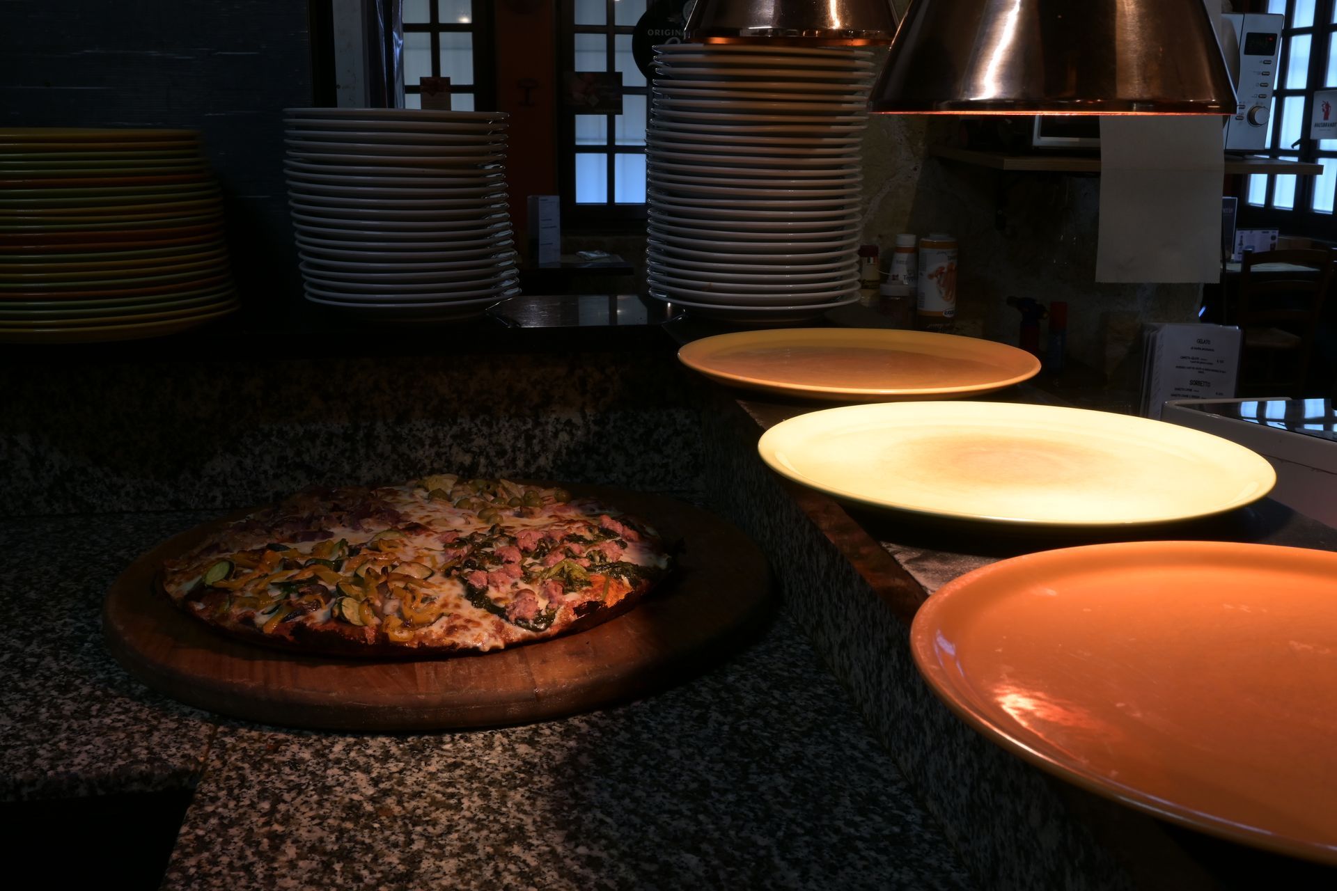 Pizza sul bancone sotto le lampade riscaldanti in una cucina di ristorante poco illuminata