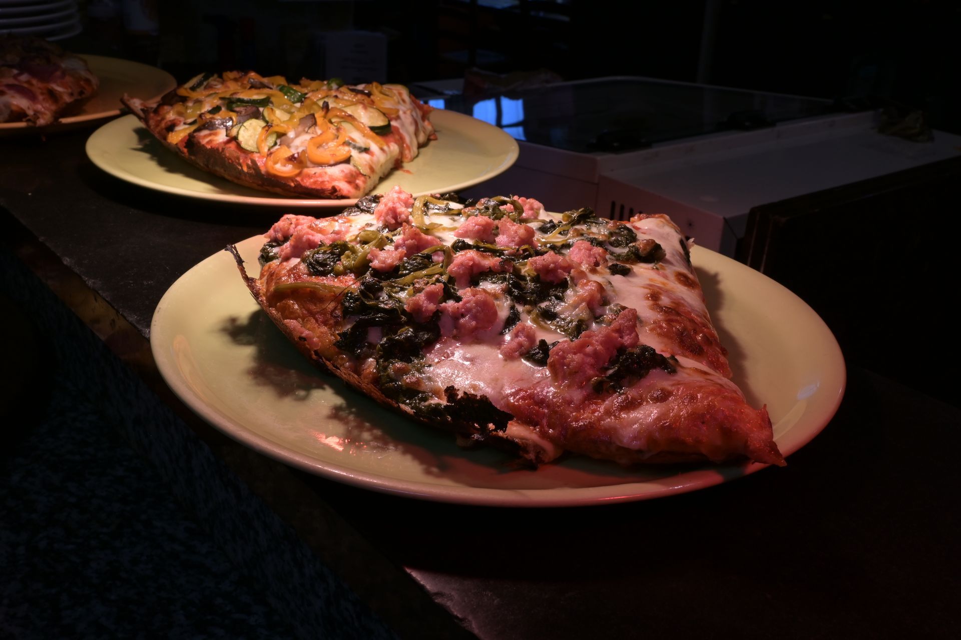 Due pizze sui piatti, una in primo piano con formaggio fuso e condimenti