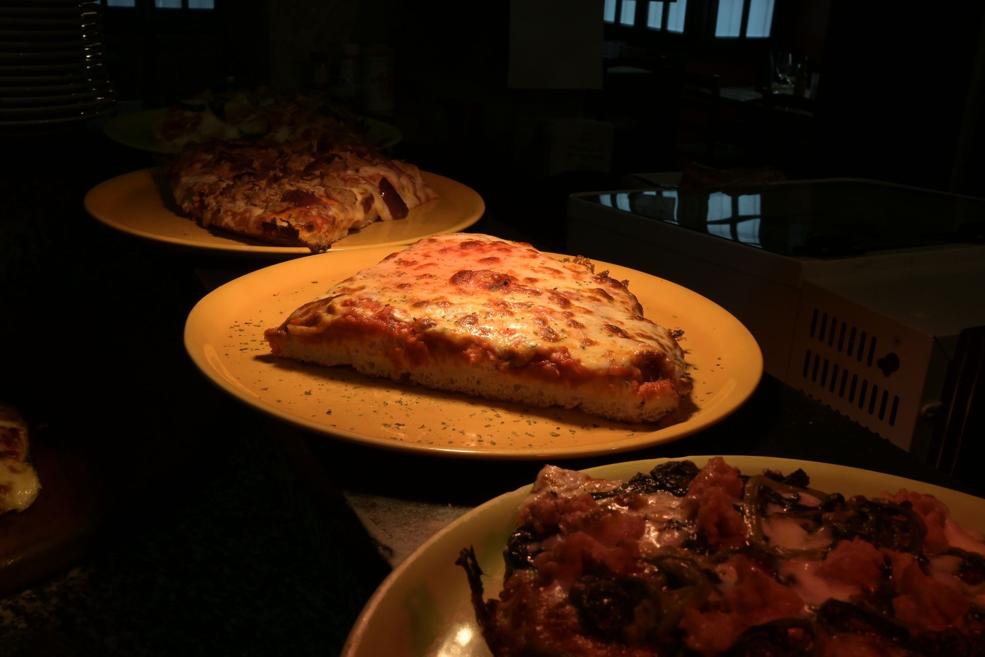 Pizze assortite sui piatti, illuminate da una luce calda in un ambiente interno buio