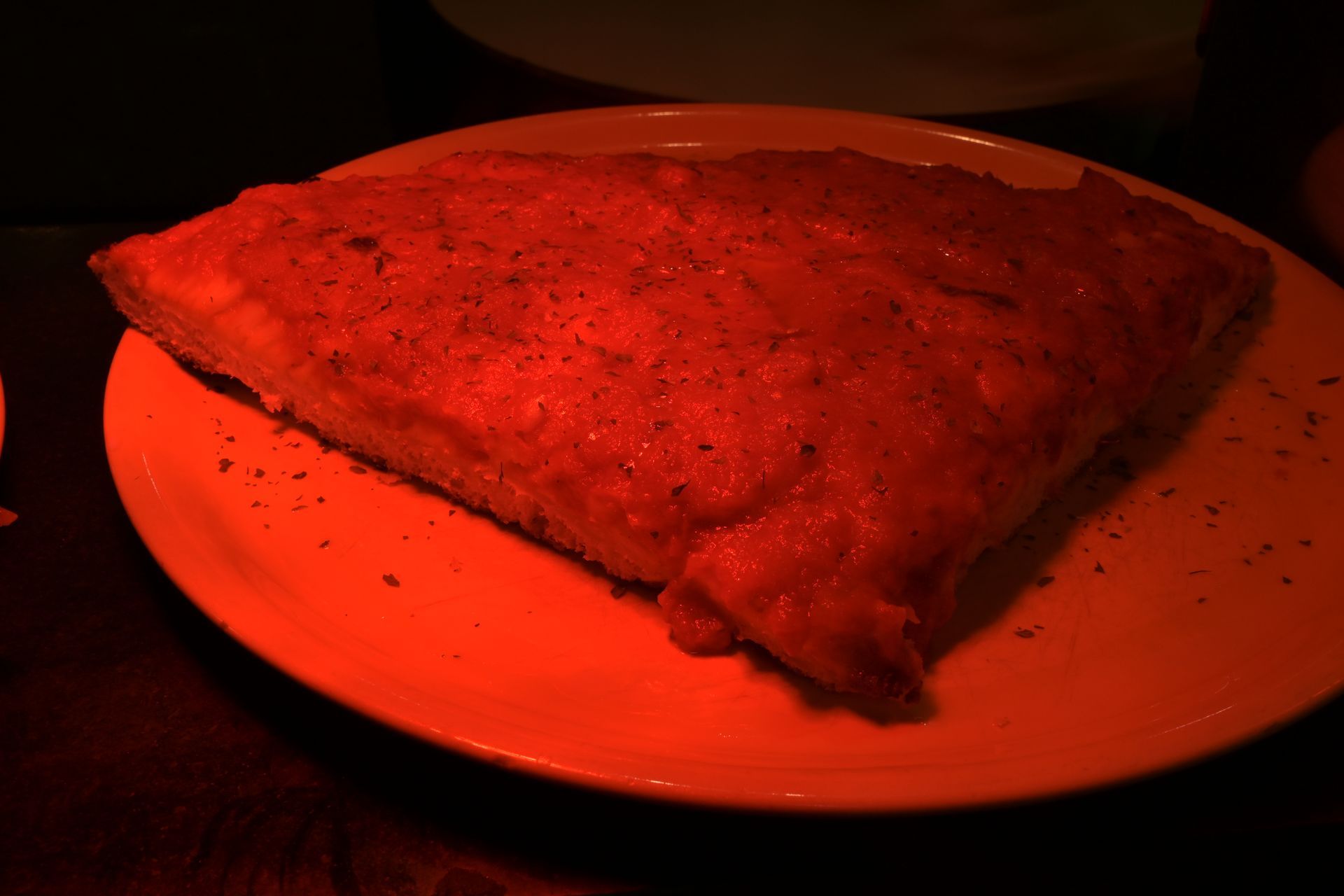 Fetta di pizza illuminata di rosso su un piatto bianco