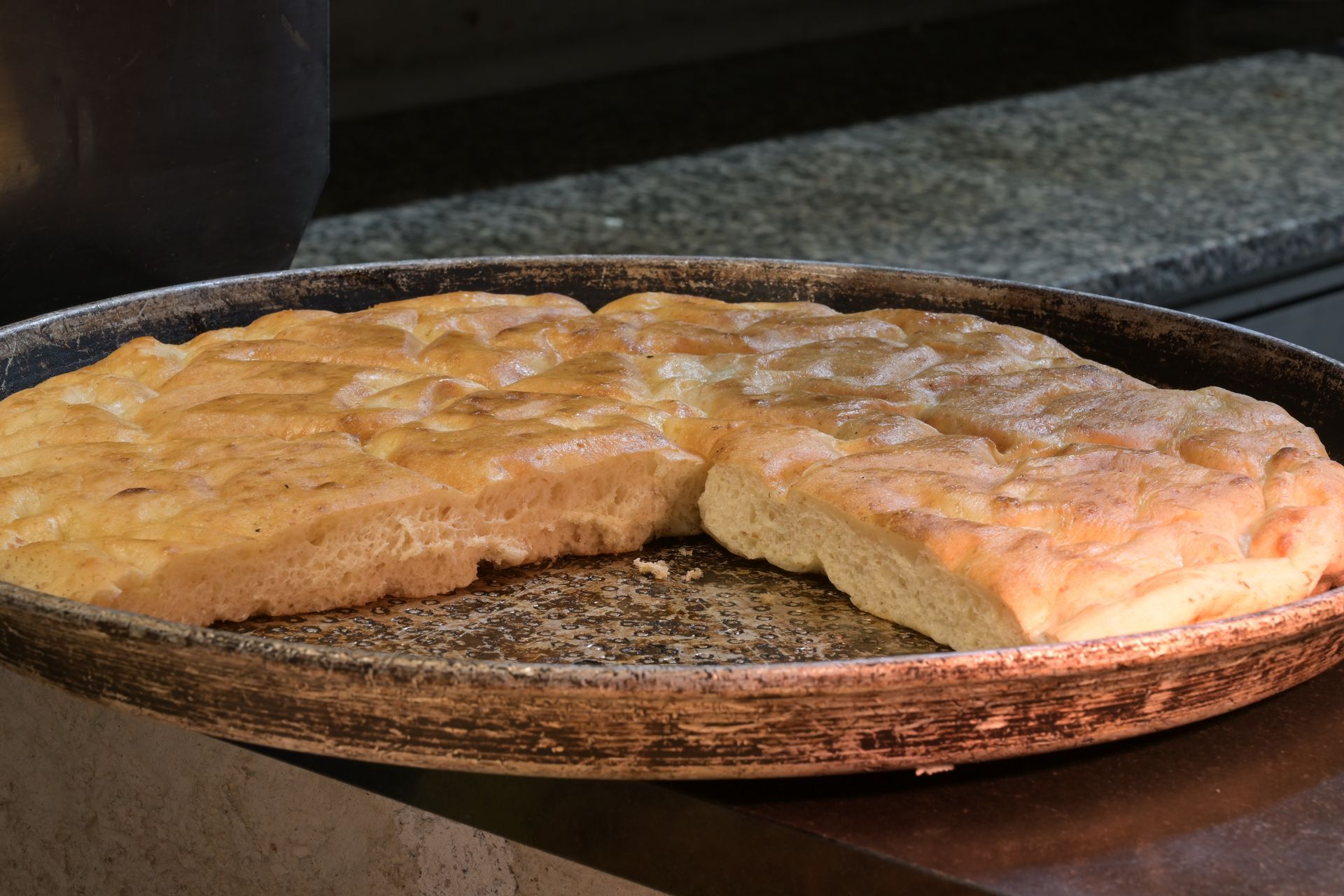 Focaccia appena sfornata su una teglia rotonda, tagliata a fette e appoggiata sul piano della cucina