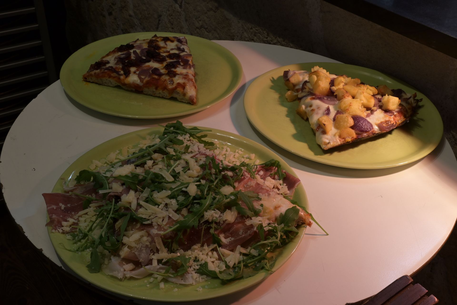 Tre piatti di pizza su piatti verdi intorno a un tavolo rotondo bianco