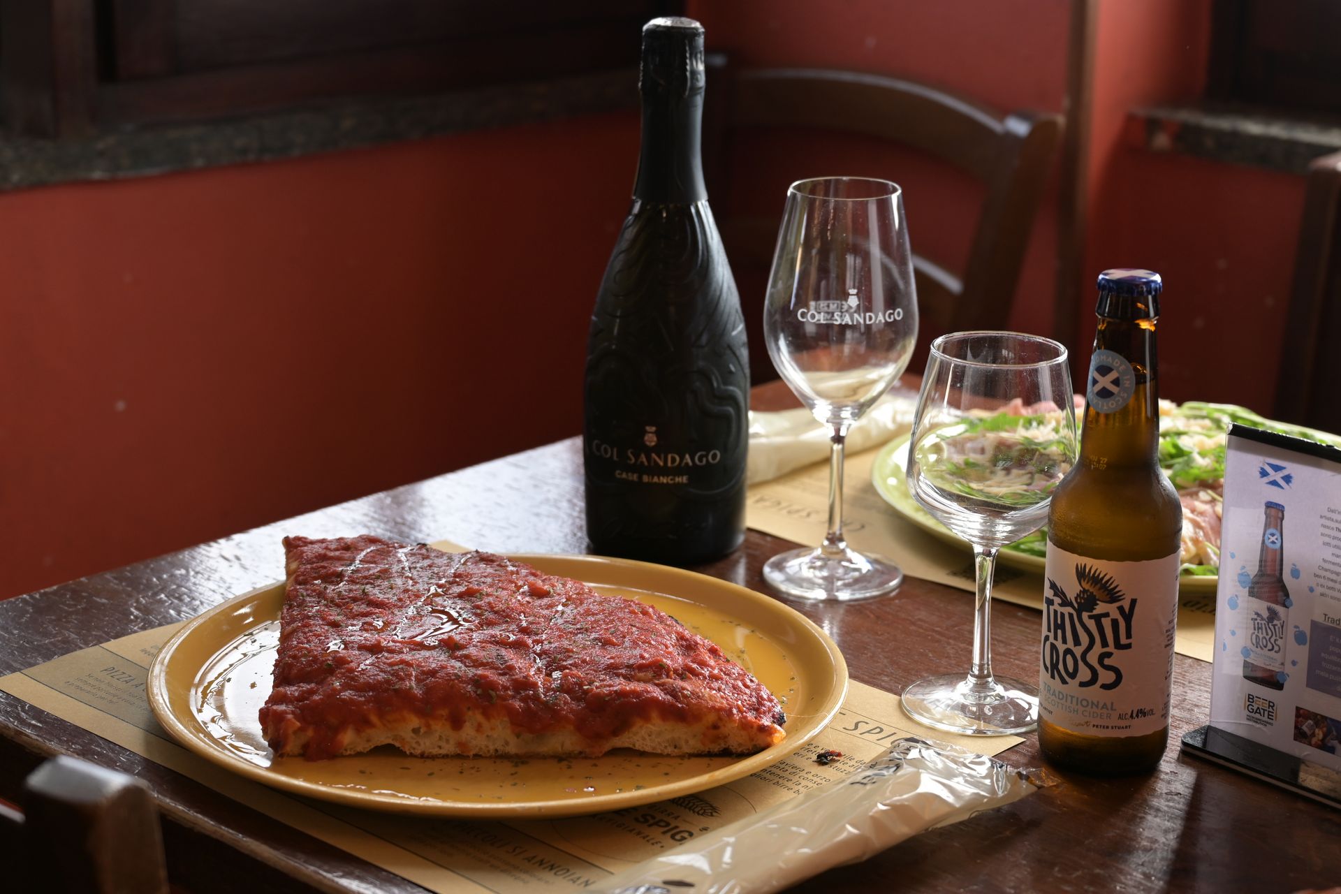 Una bottiglia di vino, dei calici e una fetta di torta impiattata su un tavolo del ristorante.