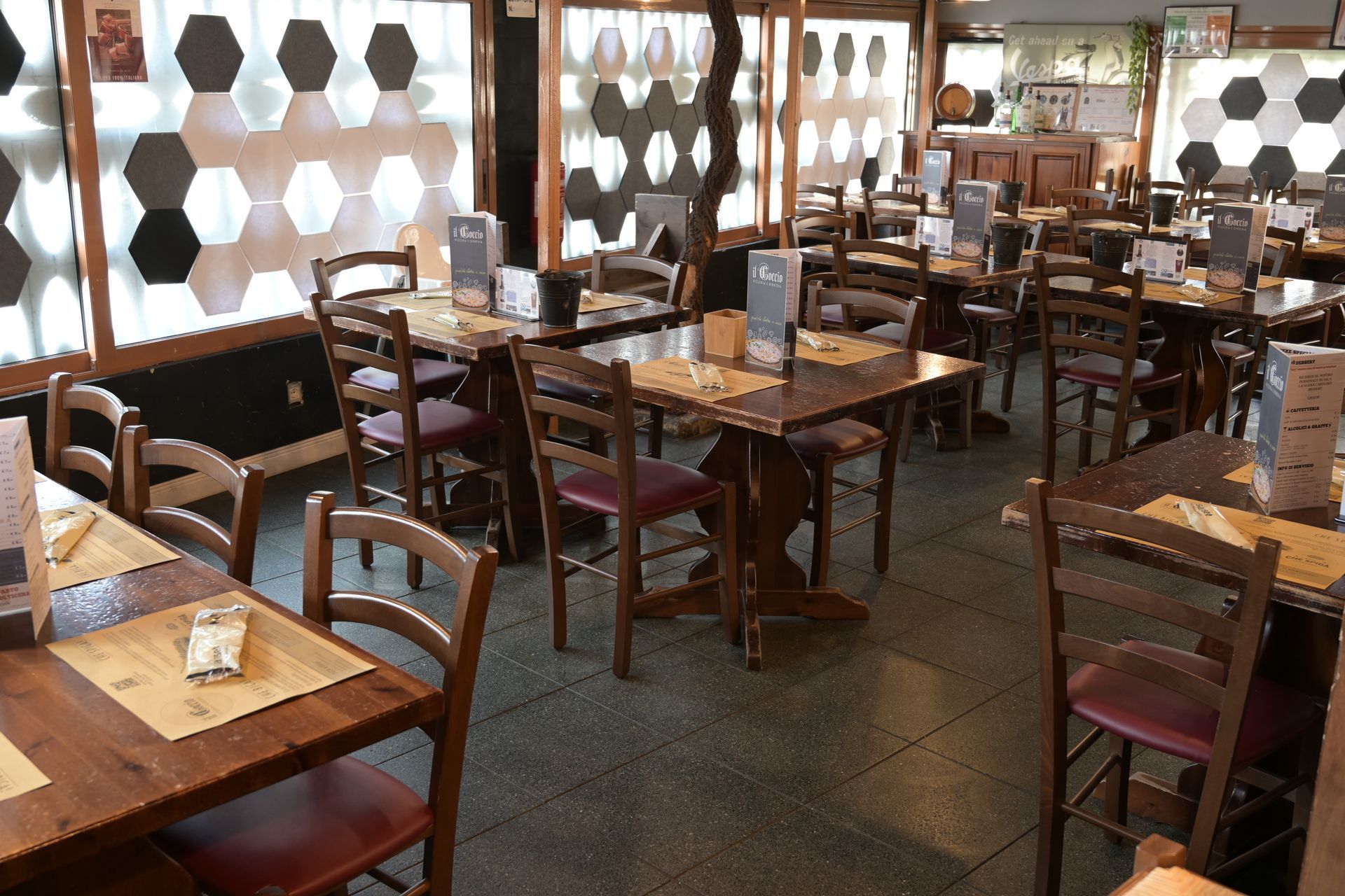 Sala da pranzo vuota di un ristorante, con tavoli e sedie in legno vicino a grandi finestre con pannelli di vetro esagonali