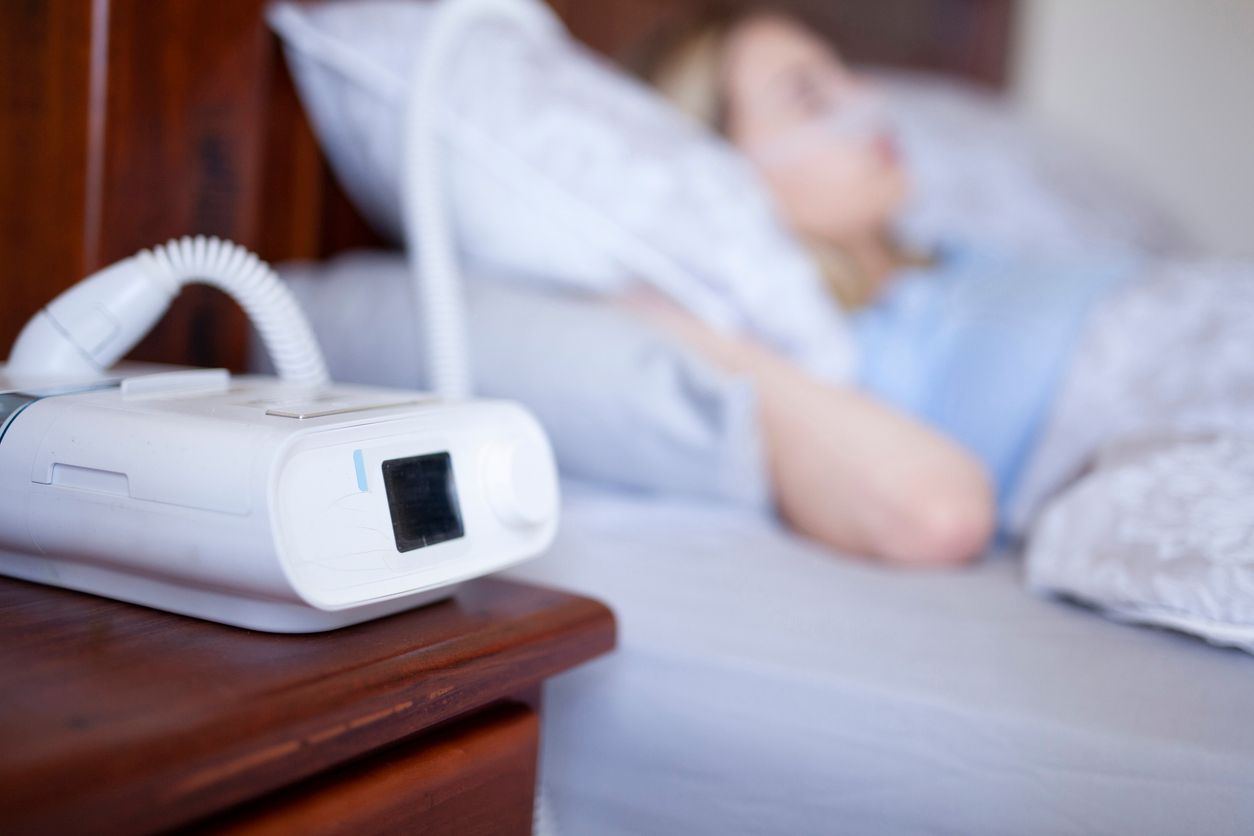 CPAP machine on bedside table beside a sleeping person in bed