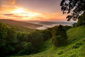 Sunrise over a lush green valley with misty hills and glowing orange sky