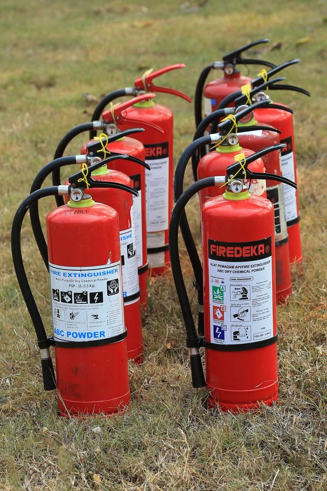 Several red fire extinguishers standing on grass outdoors, with black hoses attached.