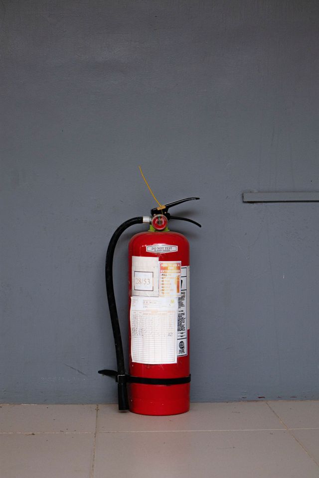 Red fire extinguisher mounted against a gray wall on a tiled floor.