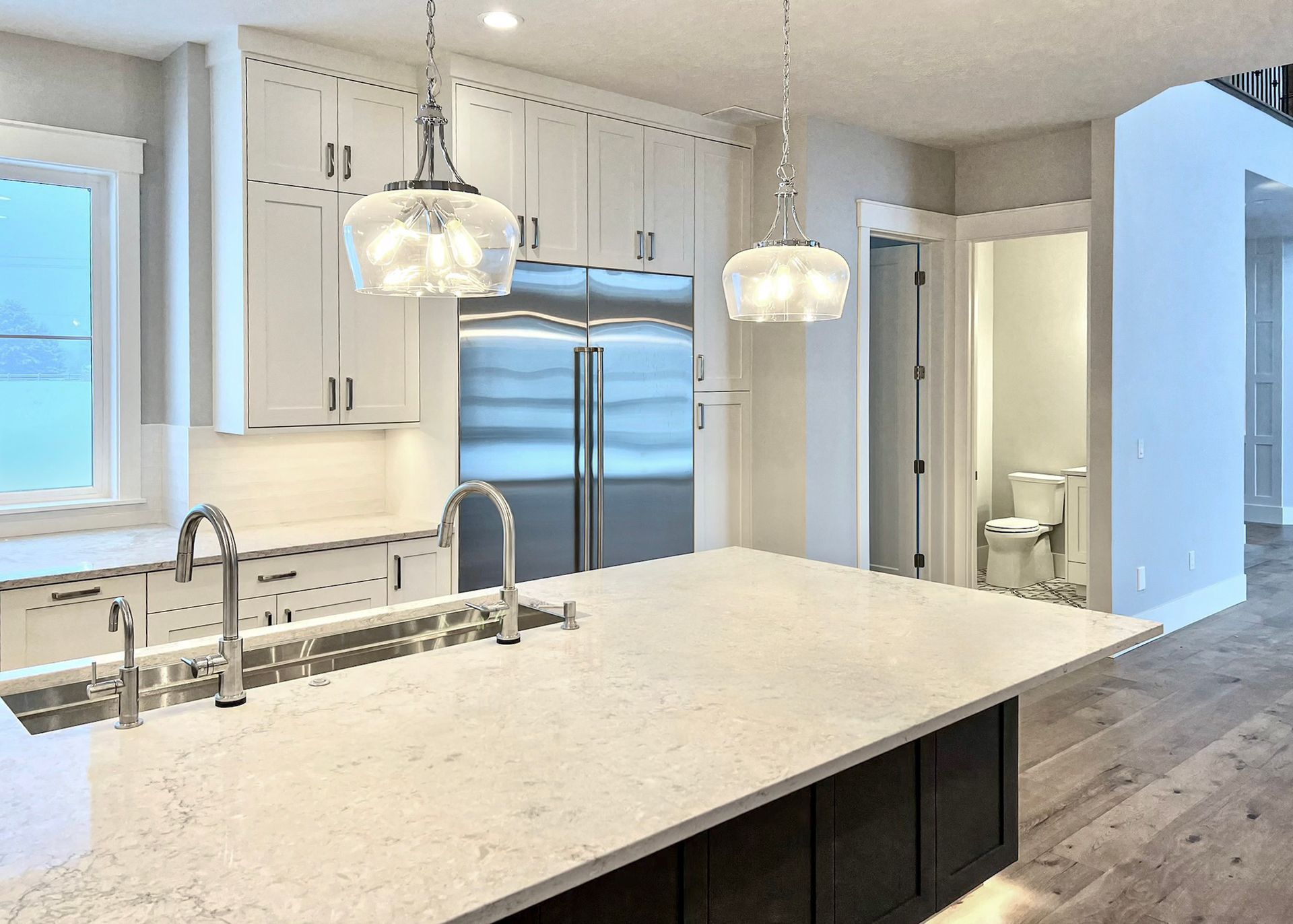 Modern white kitchen with marble island, stainless fridge, pendant lights, and wood floors