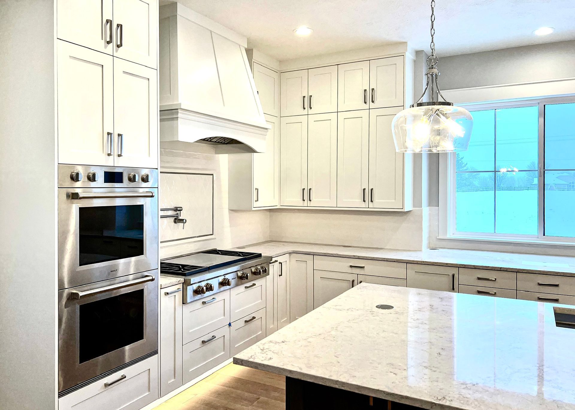 Bright white kitchen with cabinets, open shelves, patterned tile floor, and a sink under a window.