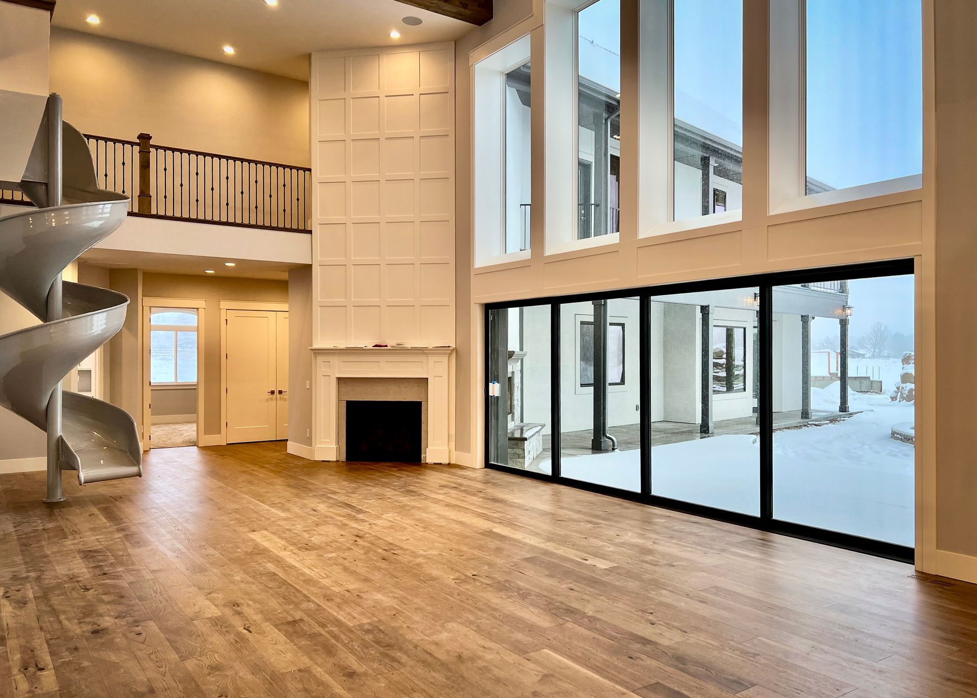 Bright open living room with hardwood floors, loft railing, fireplace, spiral staircase, and floor-to-ceiling windows