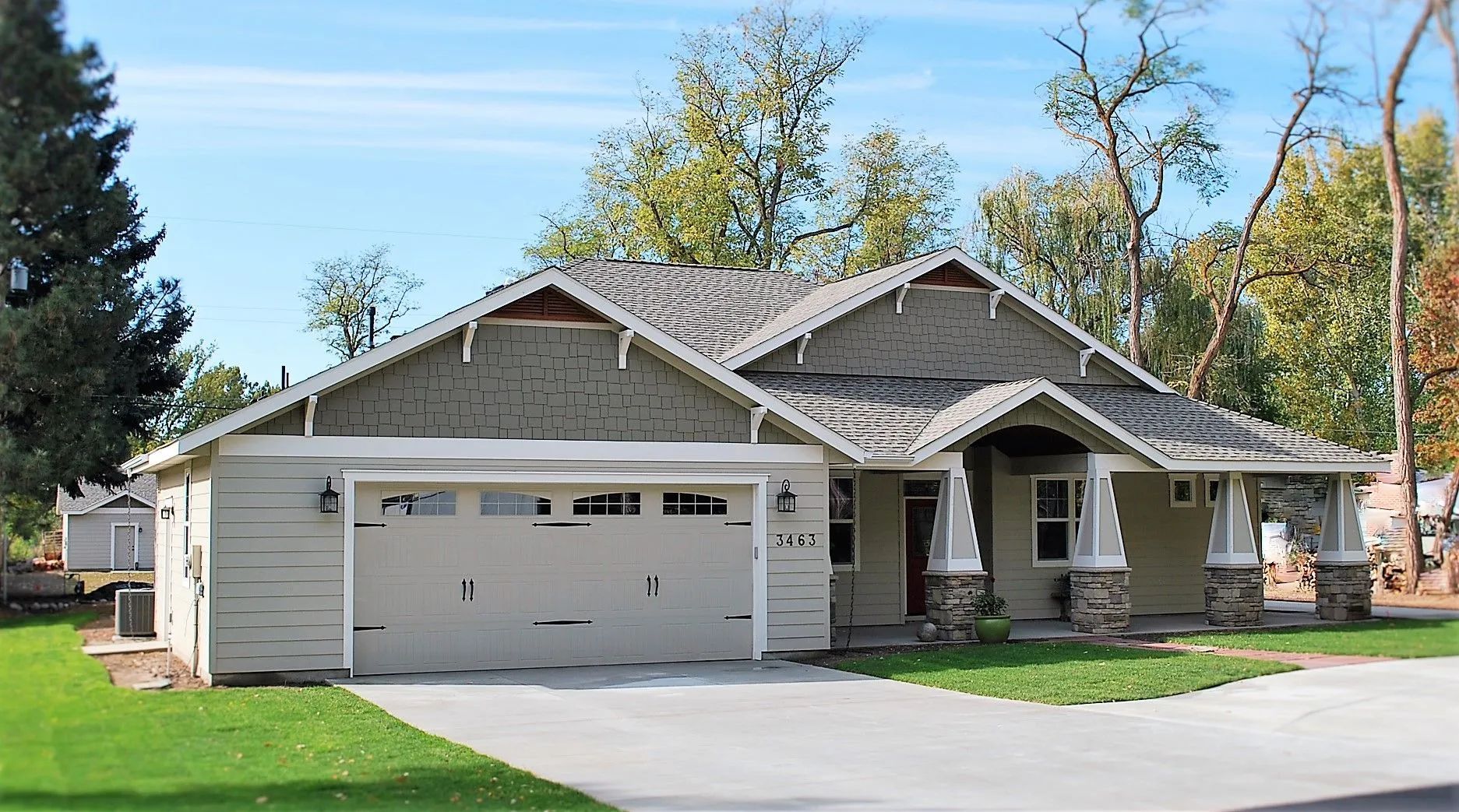 Suburban house with a gray garage, covered porch, and green lawn on a sunny day