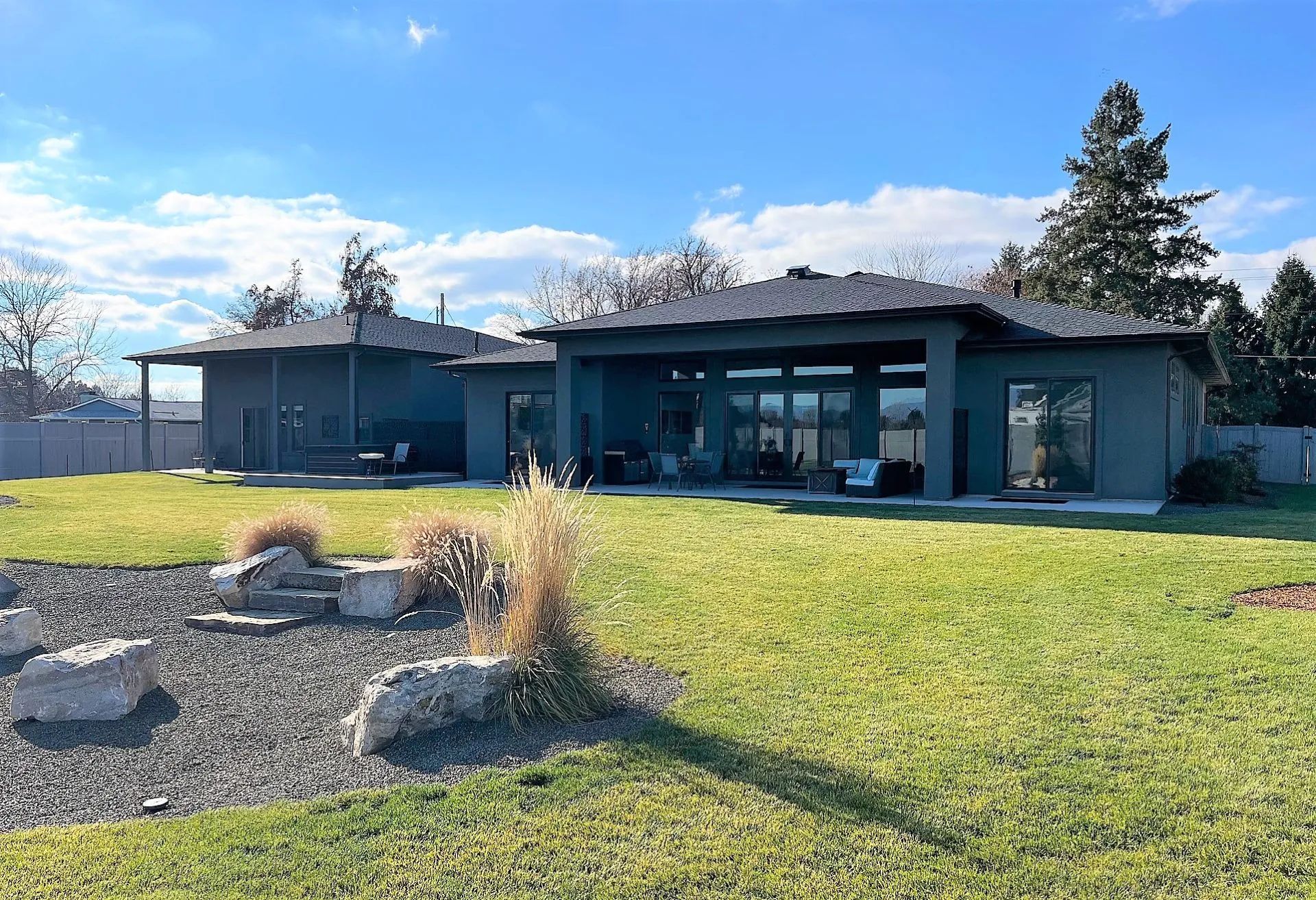 Modern single-story house with large windows, a grassy yard, and rock landscaping under a blue sky