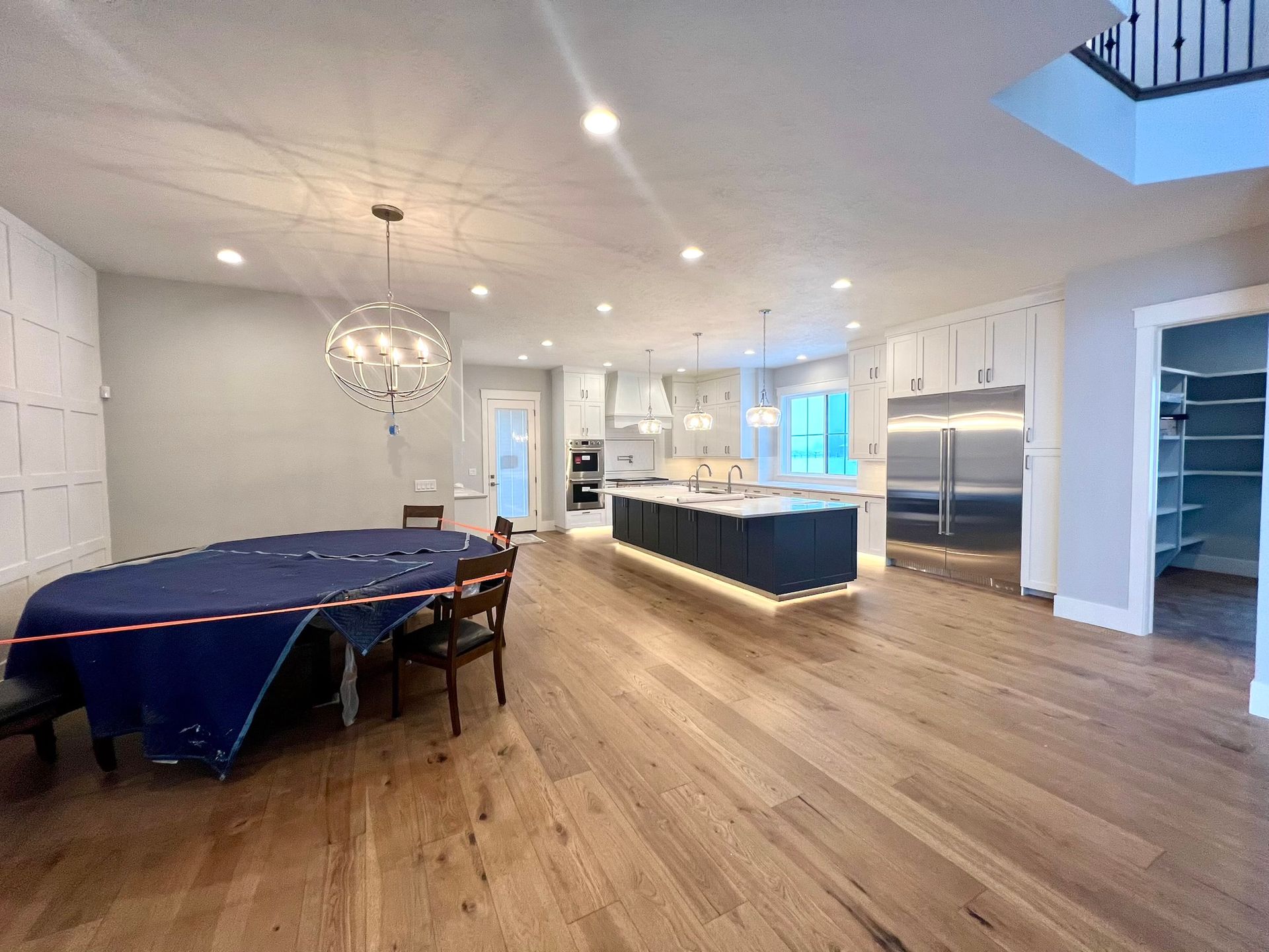 Open-concept kitchen and living space with hardwood floors, white cabinets, island, pool table, and chandelier