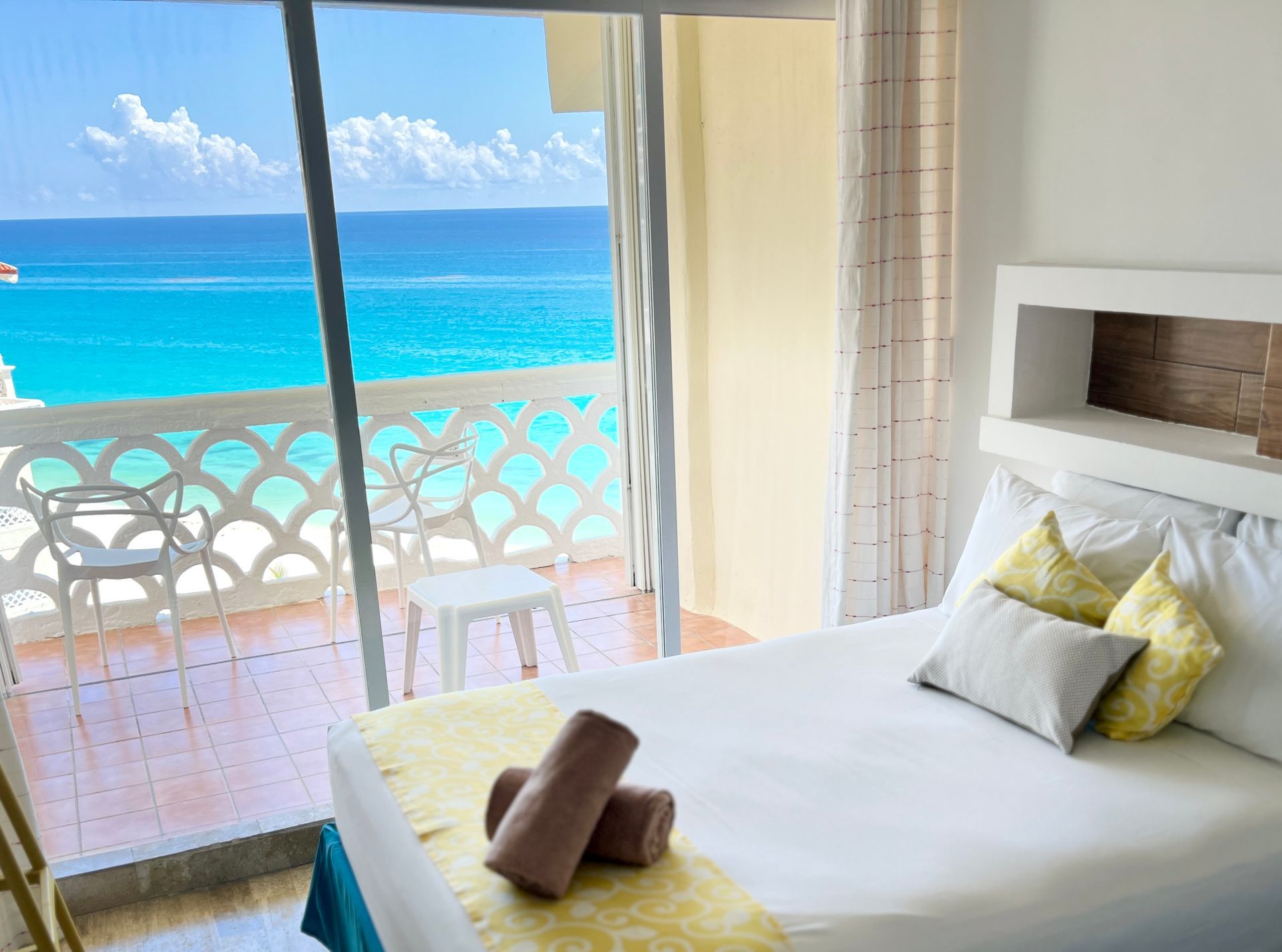 Dormitorio con vista al mar: Cama, balcón con sillas, agua turquesa.