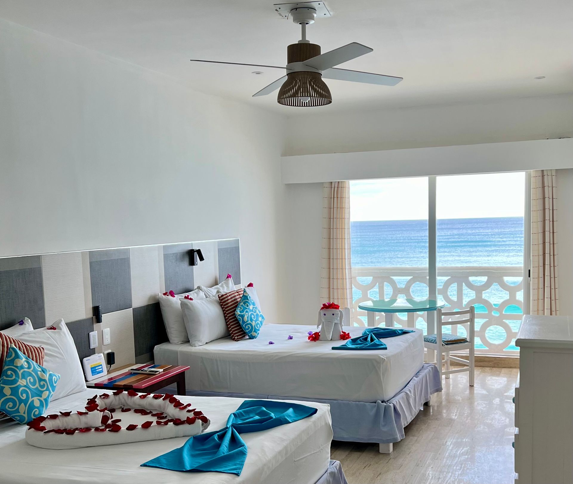 Habitación de hotel con dos camas, vista al mar, almohadas decorativas y ventilador de techo.