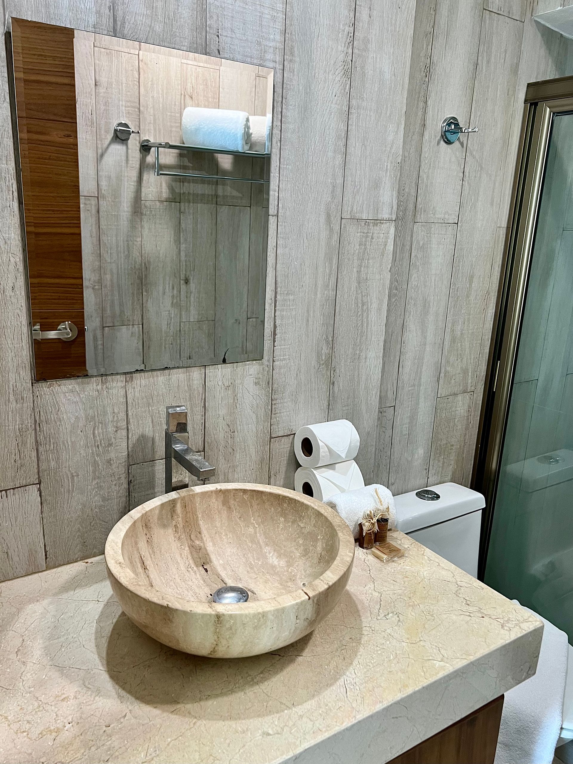 Baño con paredes y encimera de piedra, lavabo redondo y sanitario con papel higiénico.
