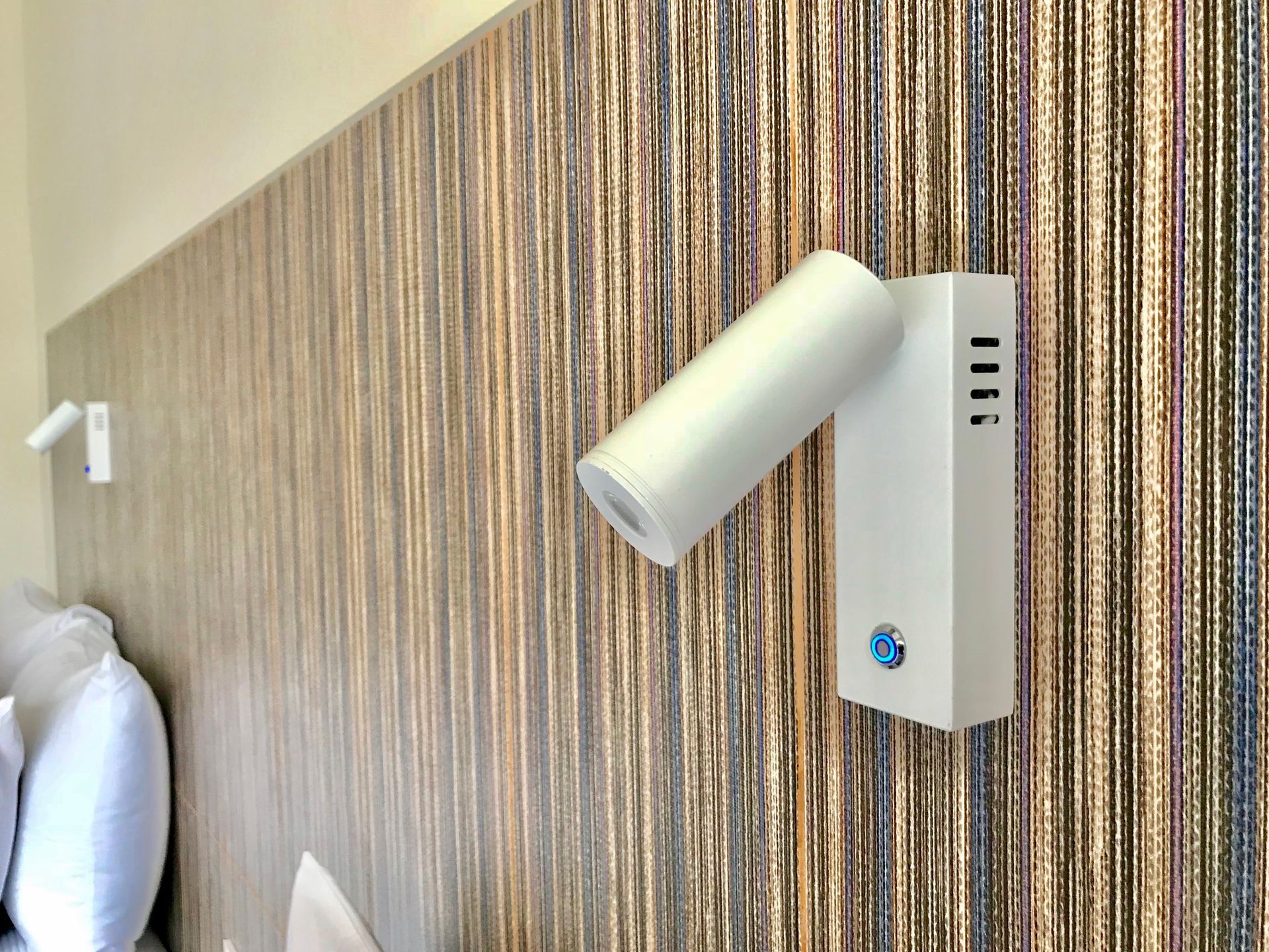 Lámpara de lectura de pared blanca con puertos USB junto a una cama con cabecero estampado.