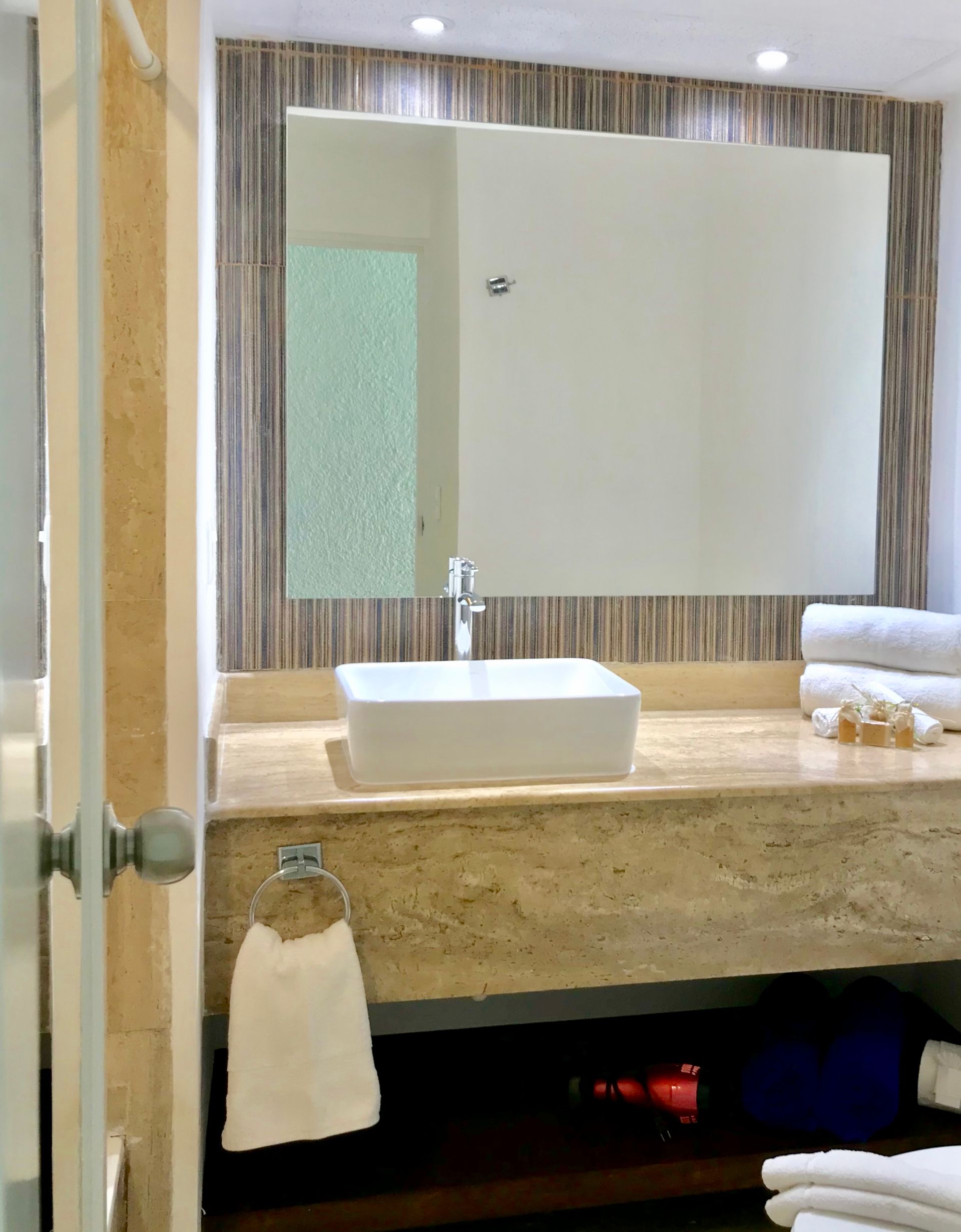 Baño con lavabo rectangular, espejo grande y toallas blancas apiladas.