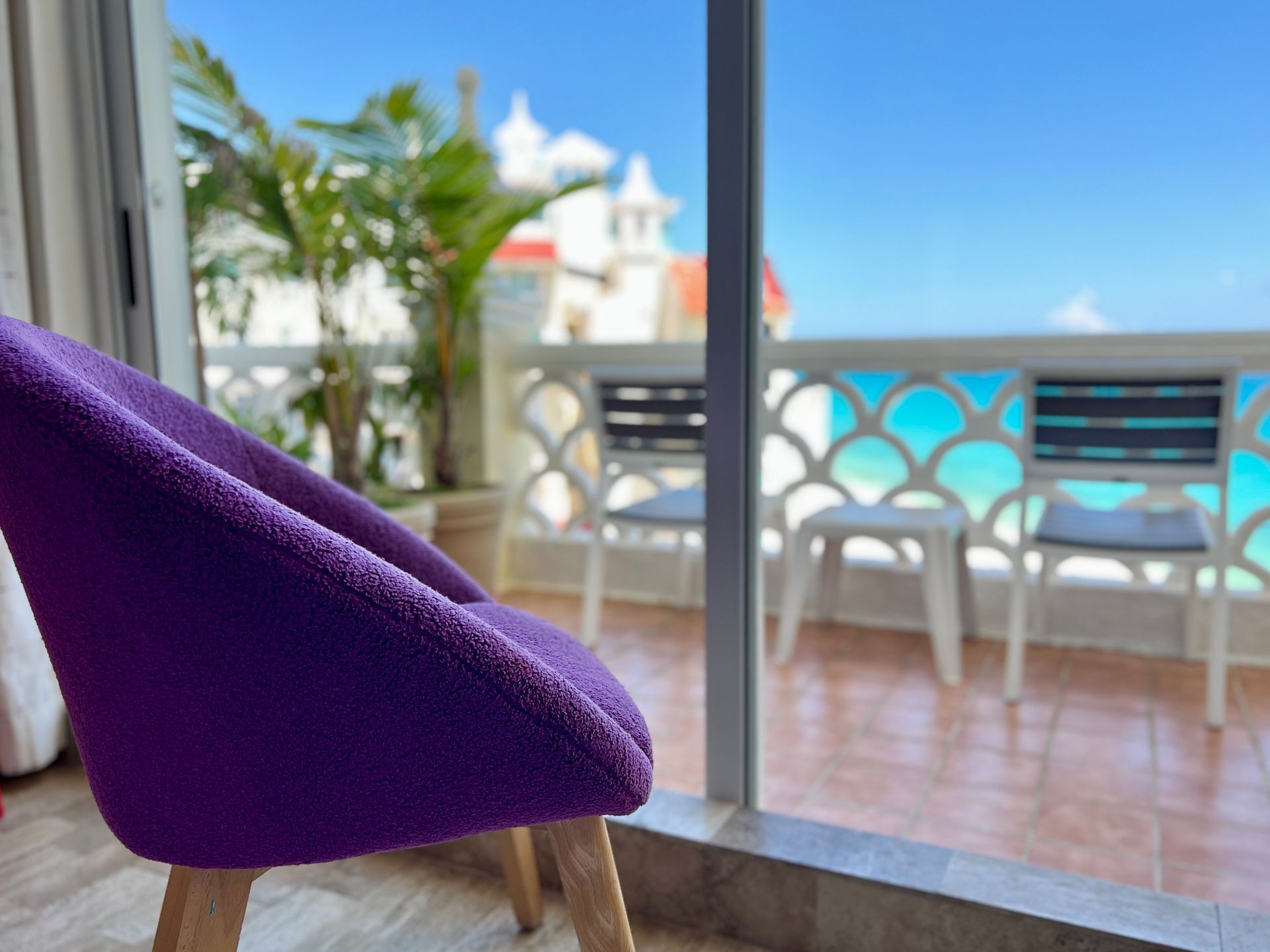 Sillón morado cerca de una puerta corrediza de vidrio con vista a un balcón con vista al mar y sillas blancas.