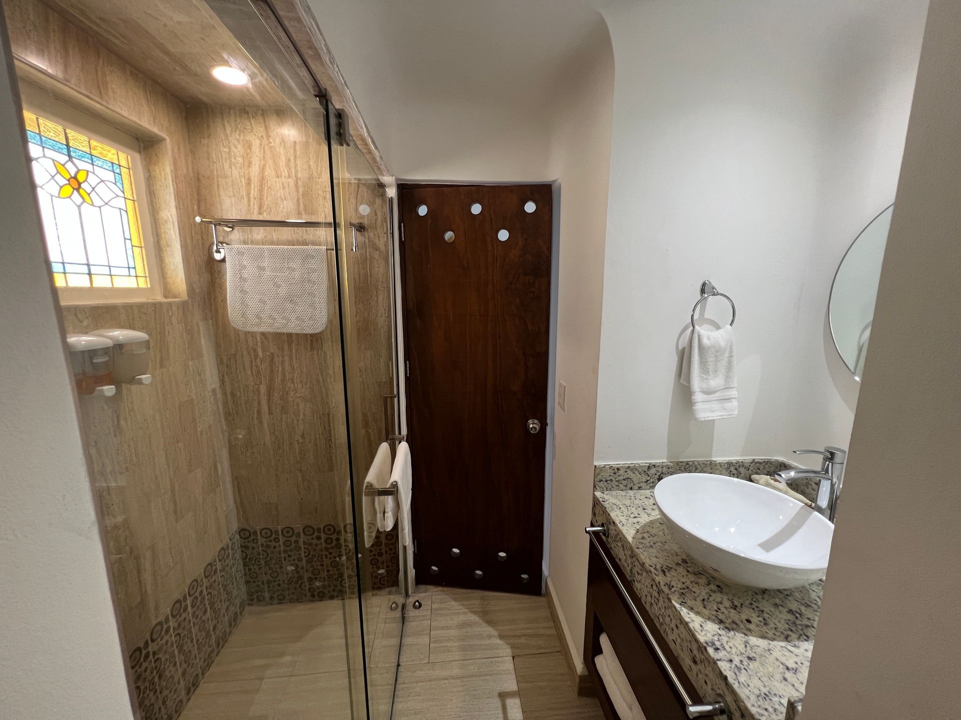 Baño con ducha, lavabo y puerta de madera. Tonos beige y marrón con vidriera.