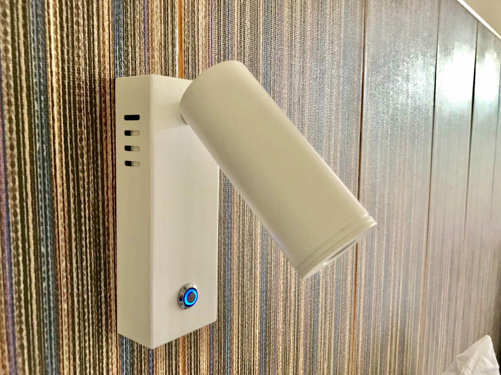 Lámpara de lectura blanca de pared con cabezal cilíndrico ajustable. Sobre una pared texturizada .