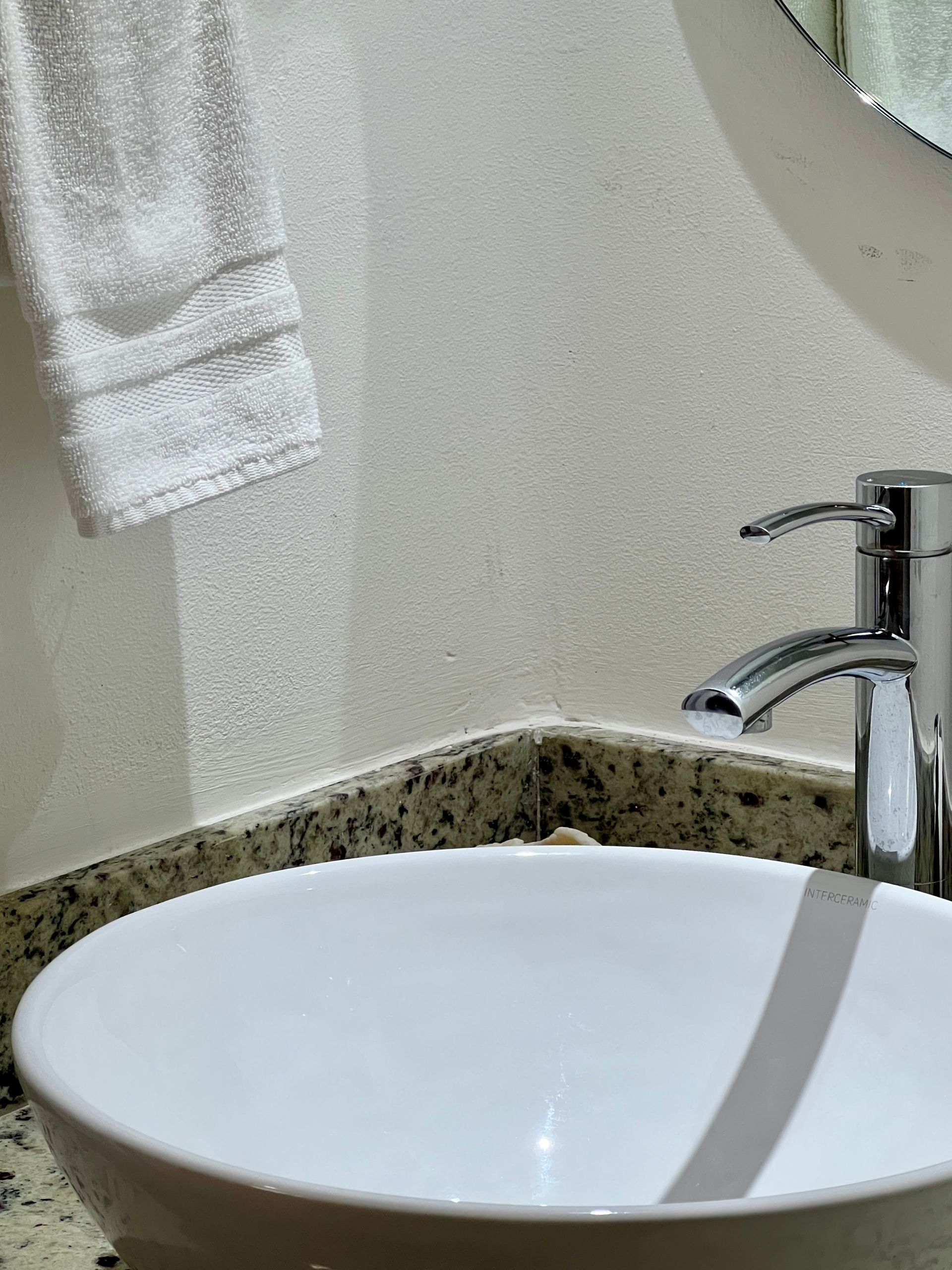 Lavabo de baño blanco con grifo cromado y una toalla blanca colgada en la pared.