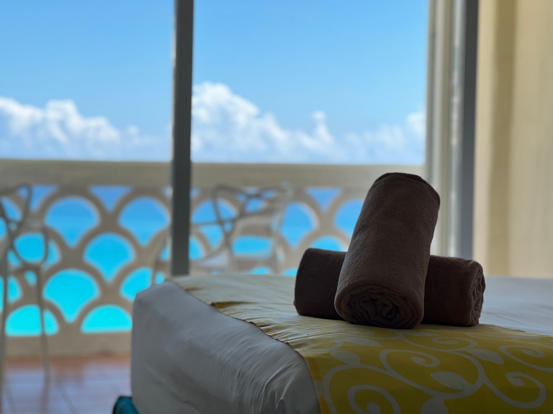 Toallas marrones enrolladas sobre una mesa de masajes, con vista a un balcón con vista al mar turquesa.
