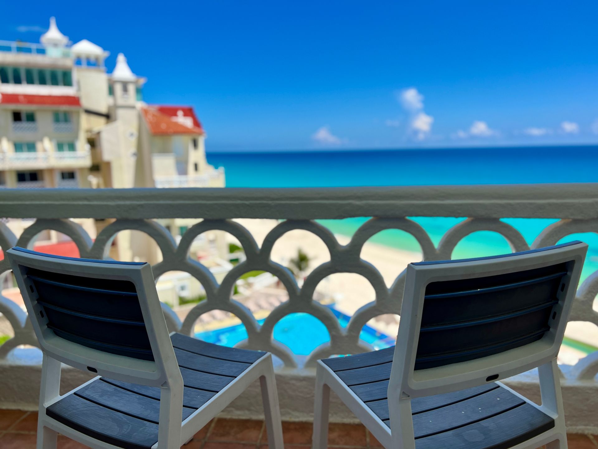 Dos sillas en un balcón con vista al mar y a un resort, cielo azul.