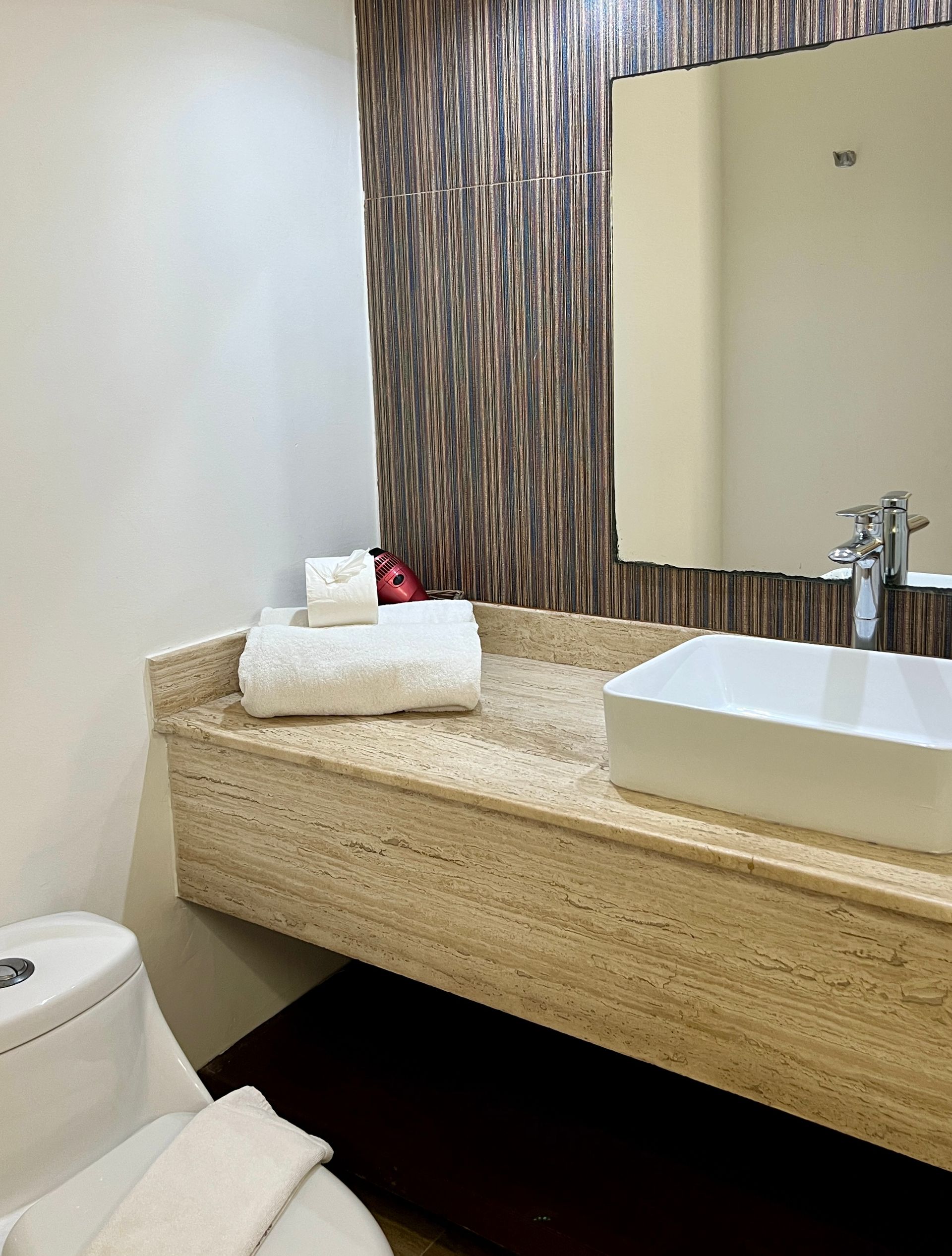 Lavabo de baño con toallas blancas, inodoro y pared texturizada.