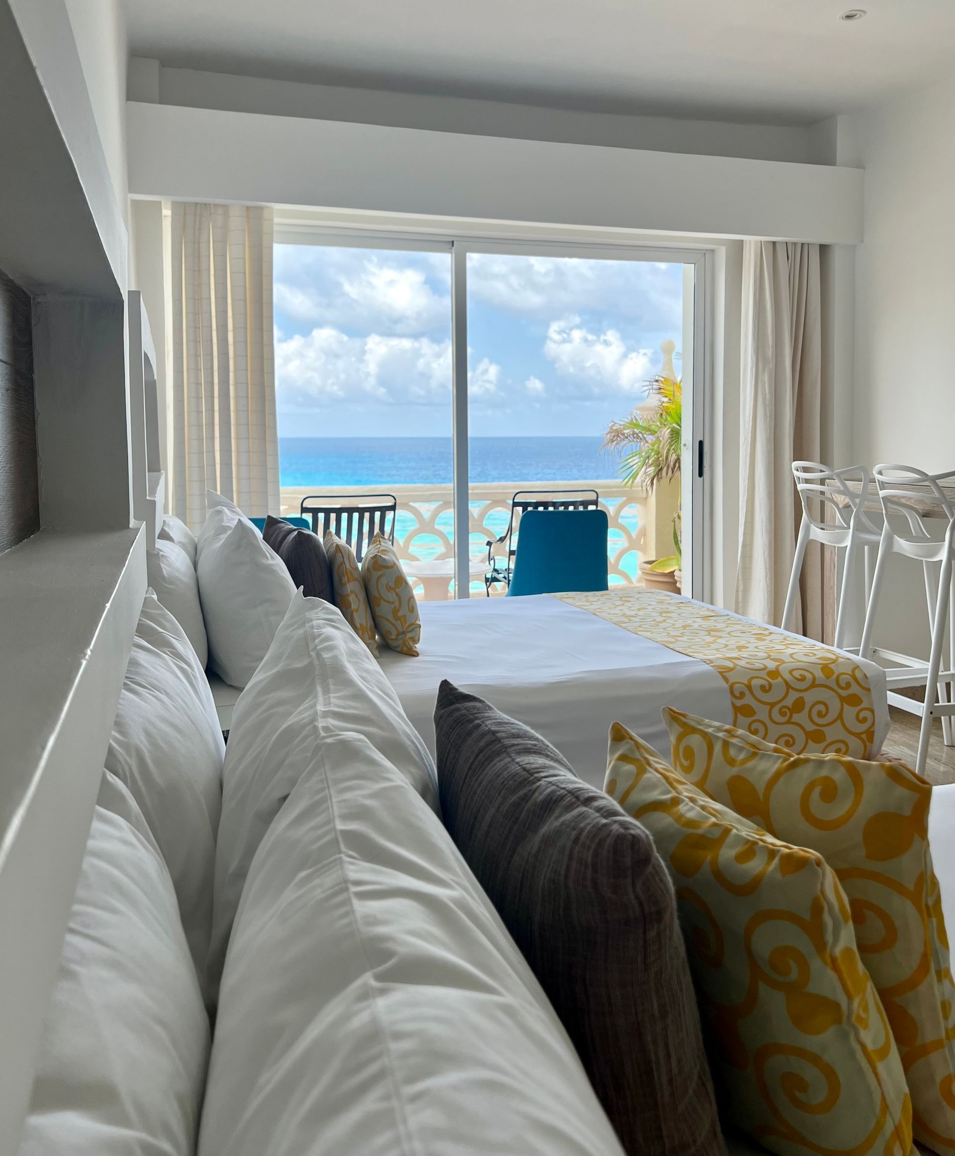 Dormitorio con dos camas, amplio ventanal con vistas al mar. Almohadas blancas, amarillas y marrones.