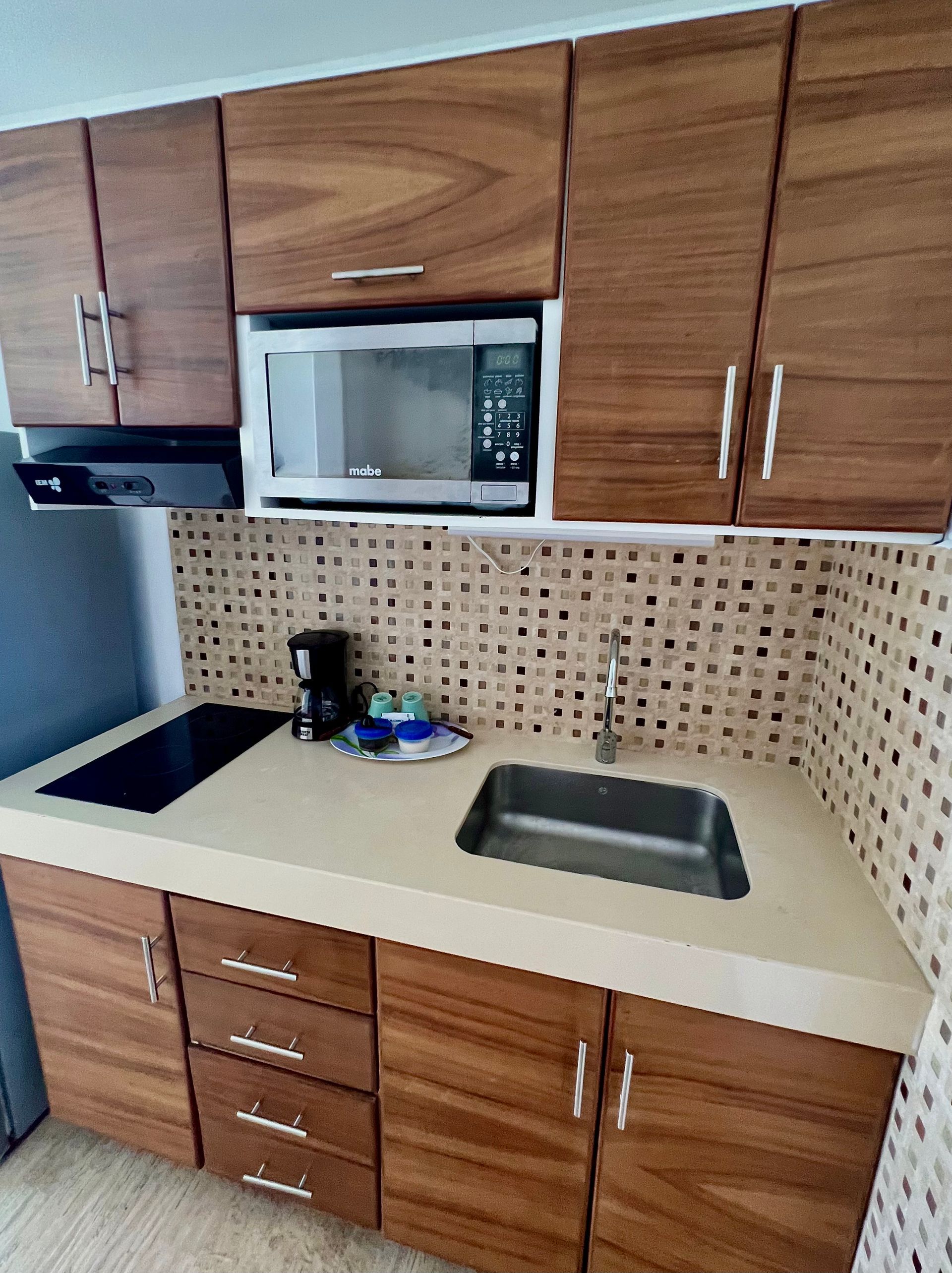 Pequeña cocina con gabinetes de madera, microondas, fregadero y estufa.