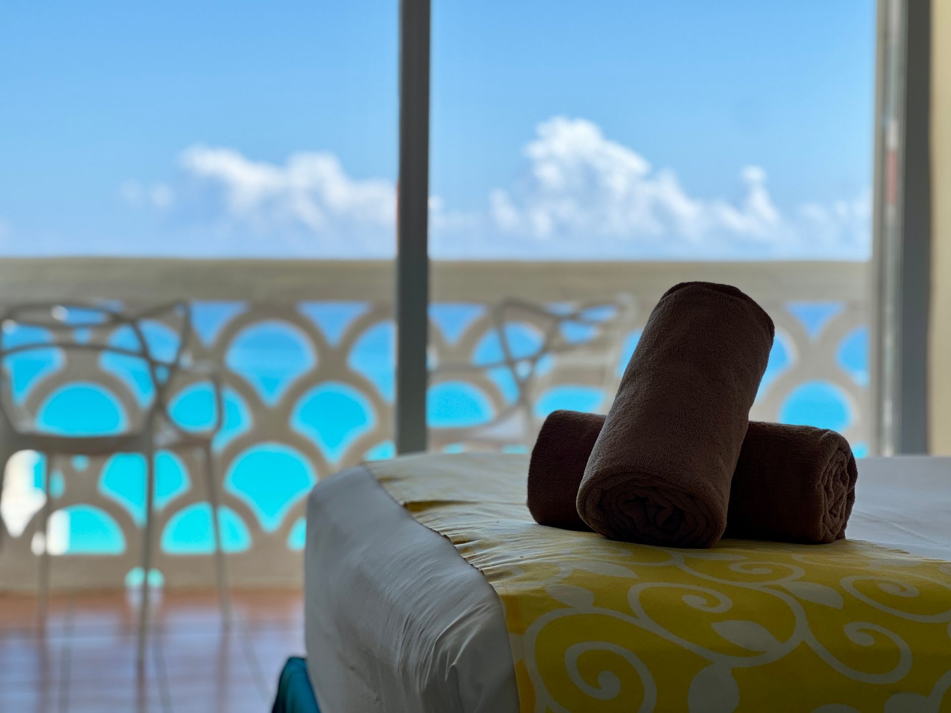 Toallas marrones enrolladas sobre la cama con vista al mar azul a través de un balcón decorativo.