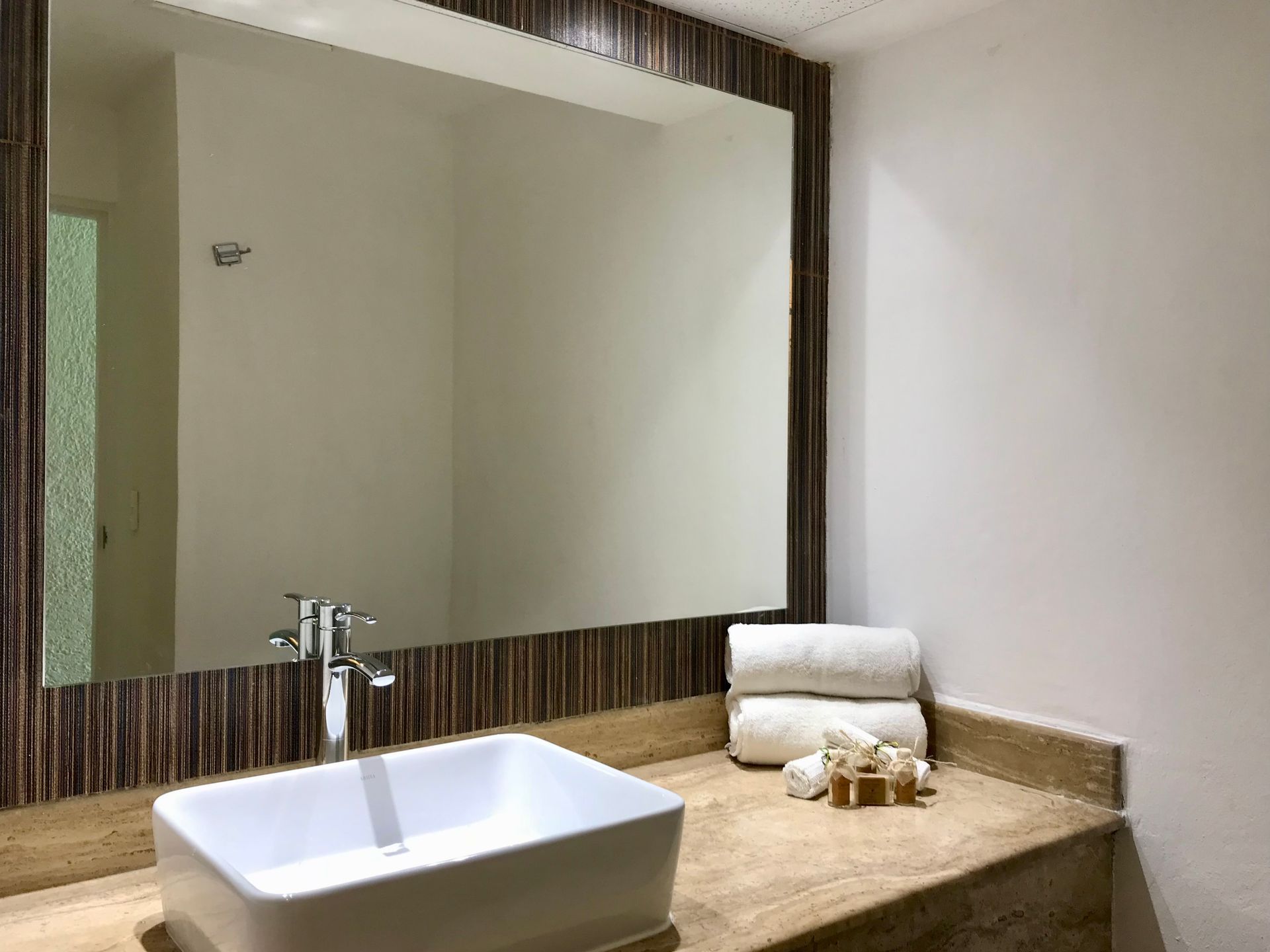 Baño con lavabo rectangular blanco, espejo grande, toallas y artículos de aseo.