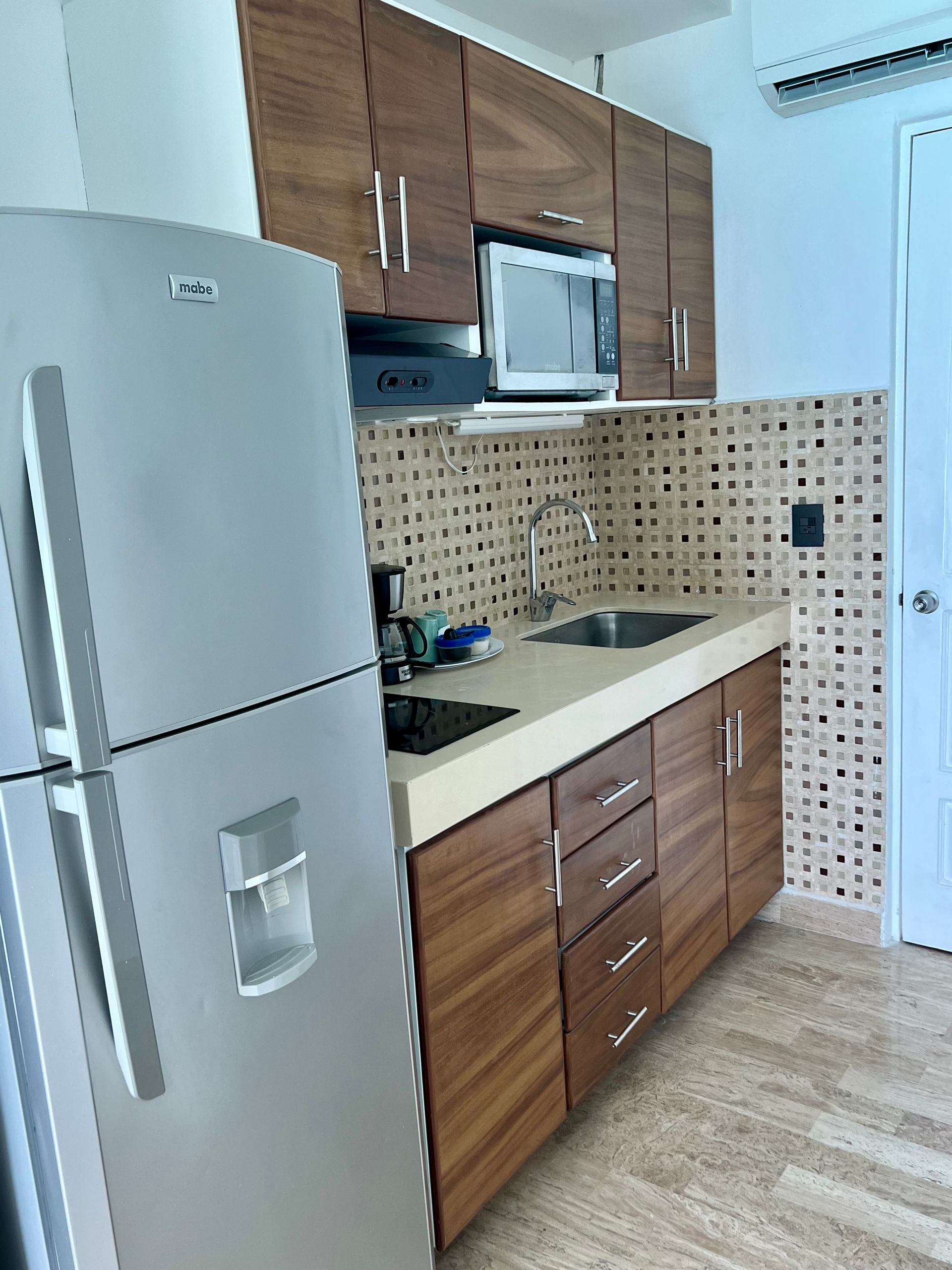 Cocina con gabinetes de madera, electrodomésticos de acero inoxidable y protector contra salpicaduras de color beige.