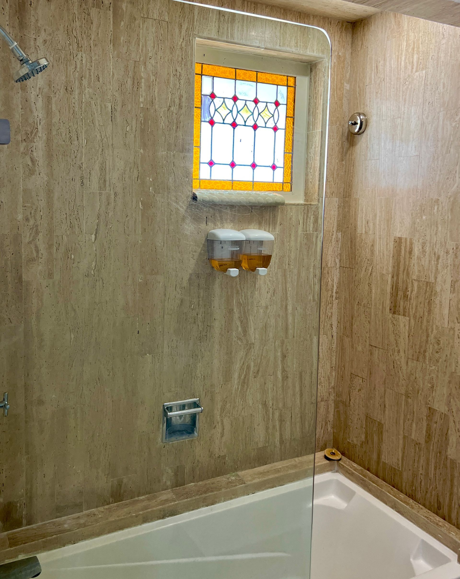 Baño con paredes de azulejos de color tostado, vidriera y ducha.