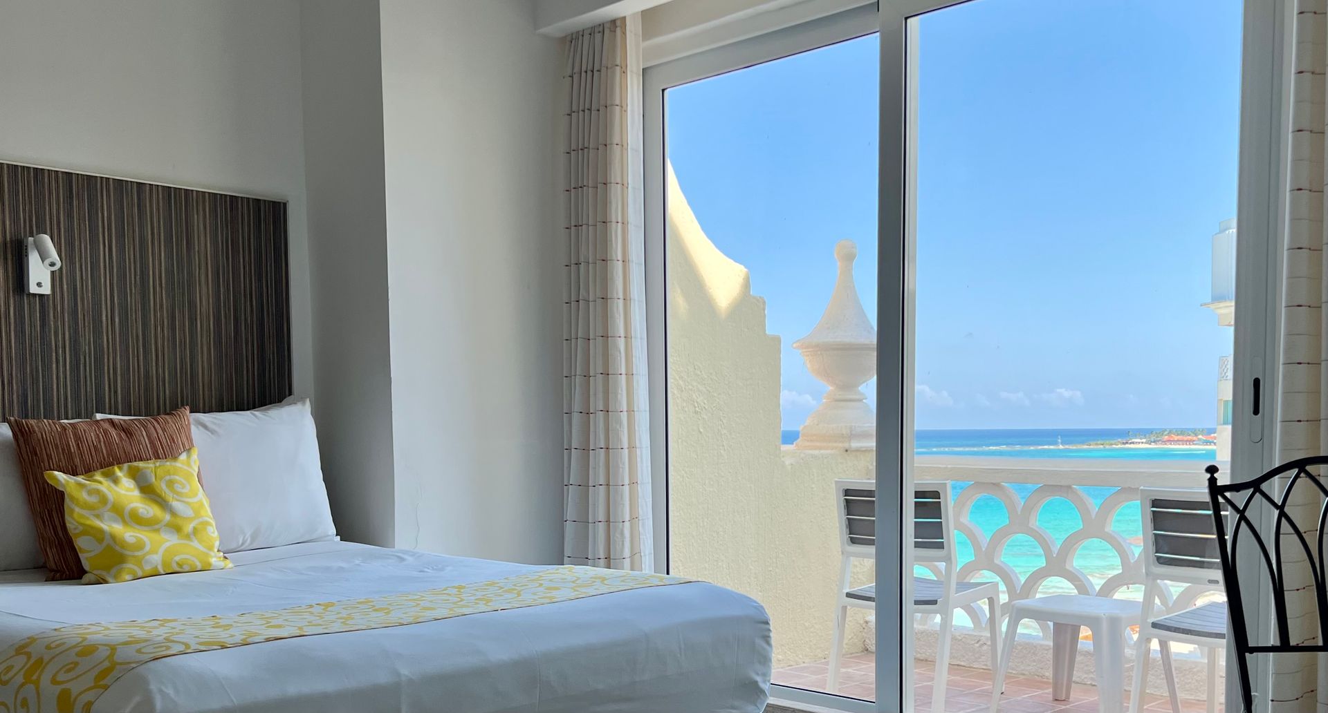 Dormitorio con cama, almohadas y un gran ventanal con vista al mar.